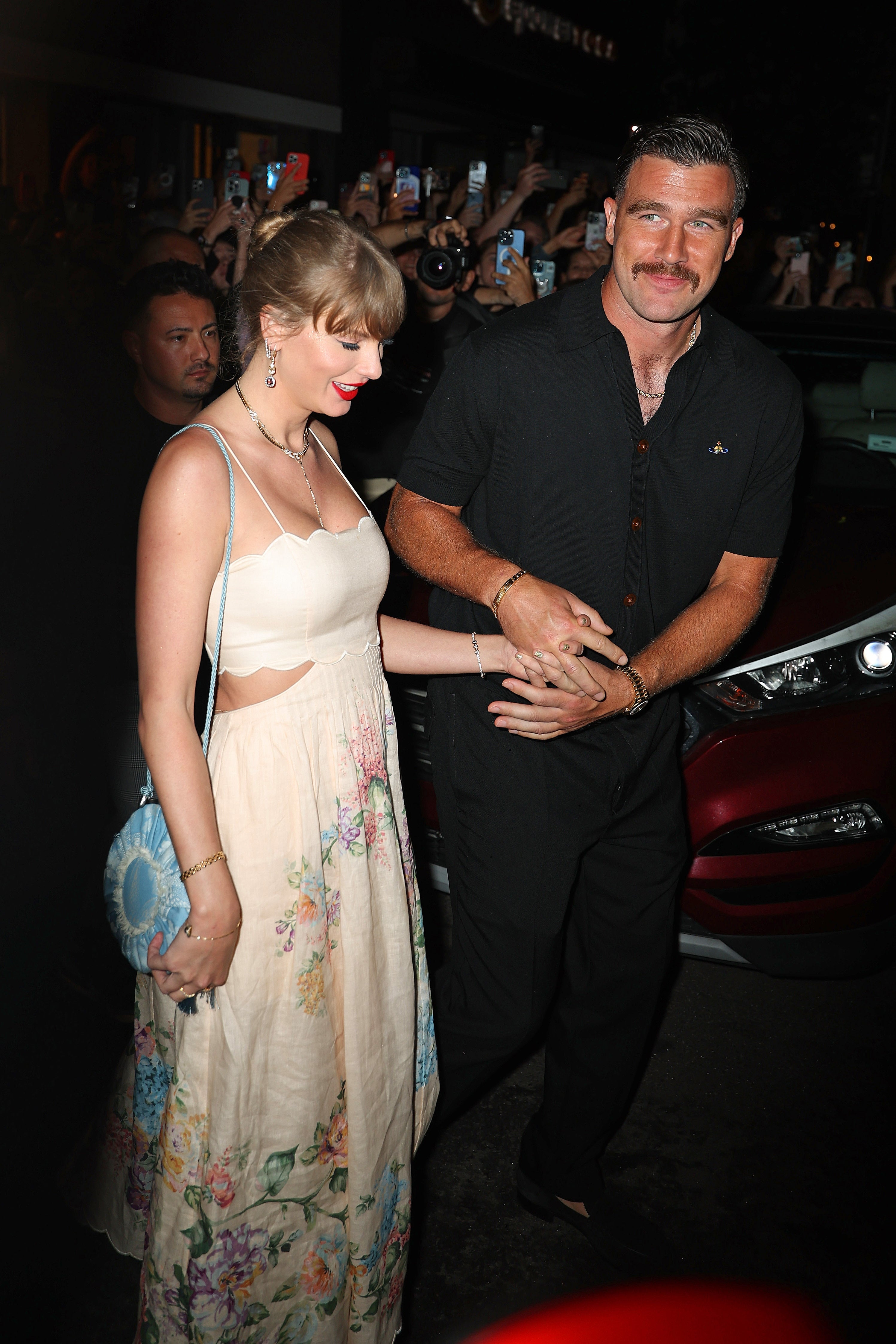 Taylor Swift successful a floral formal and Travis Kelce successful a garment and pants walking together, surrounded by fans and photographers