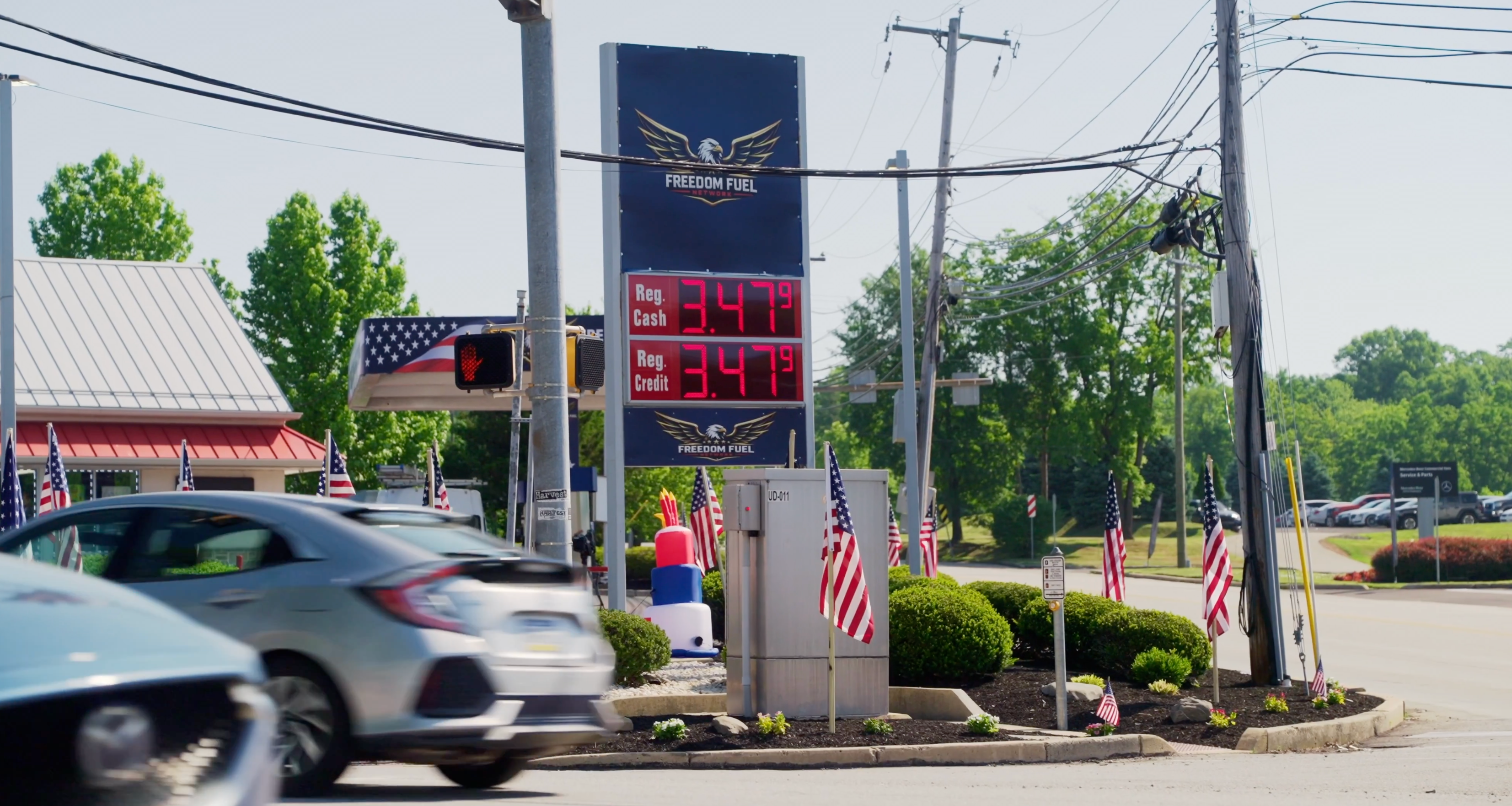Bensinstasjon med prisskilt som viser $3,47 per gallon for vanlig drivstoff. Flere amerikanske flagg er rundt stasjonen