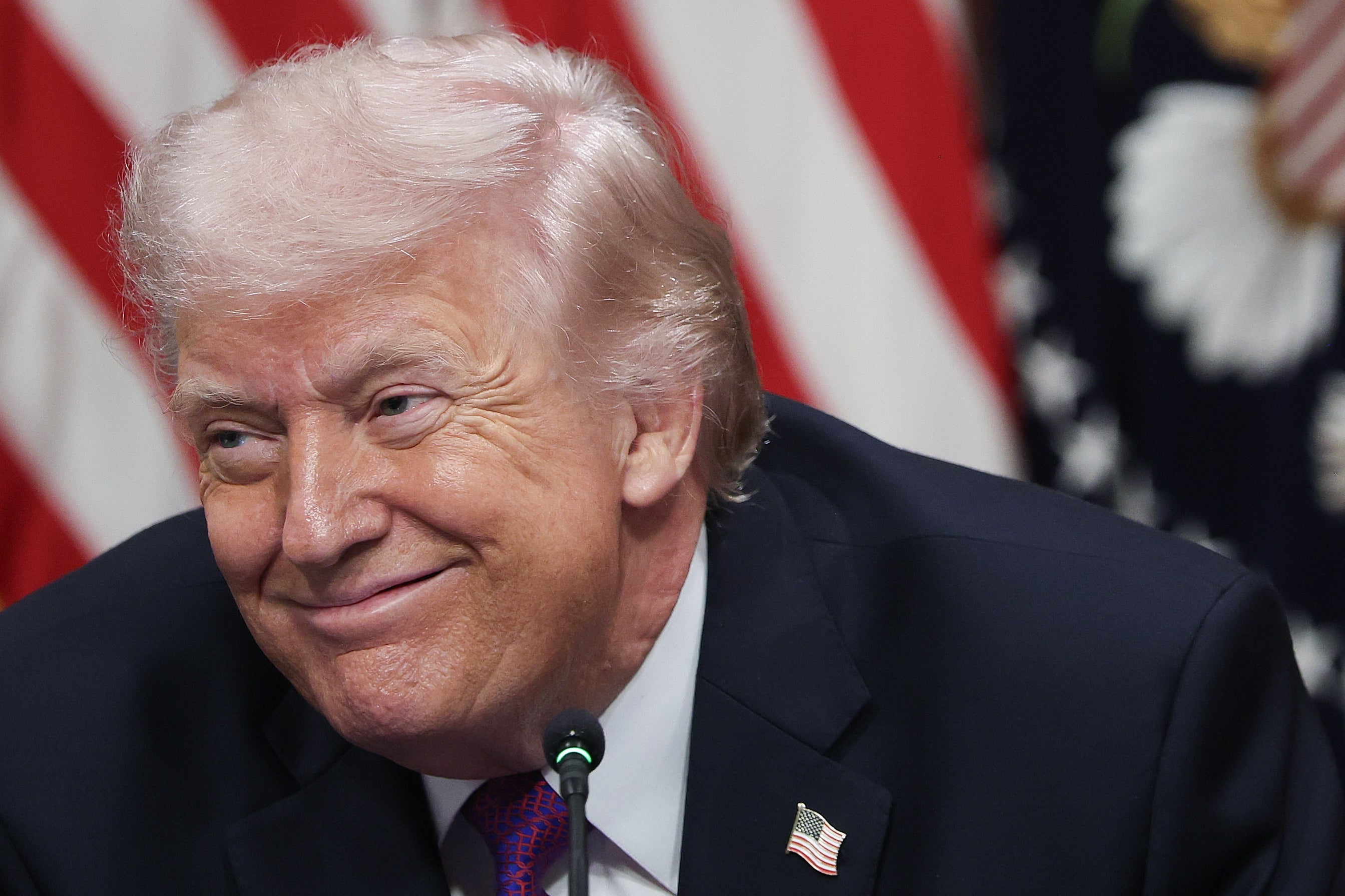 Jeg vet ikke hvem dette er, men bildet viser en person i dress som smiler med amerikanske flagg i bakgrunnen