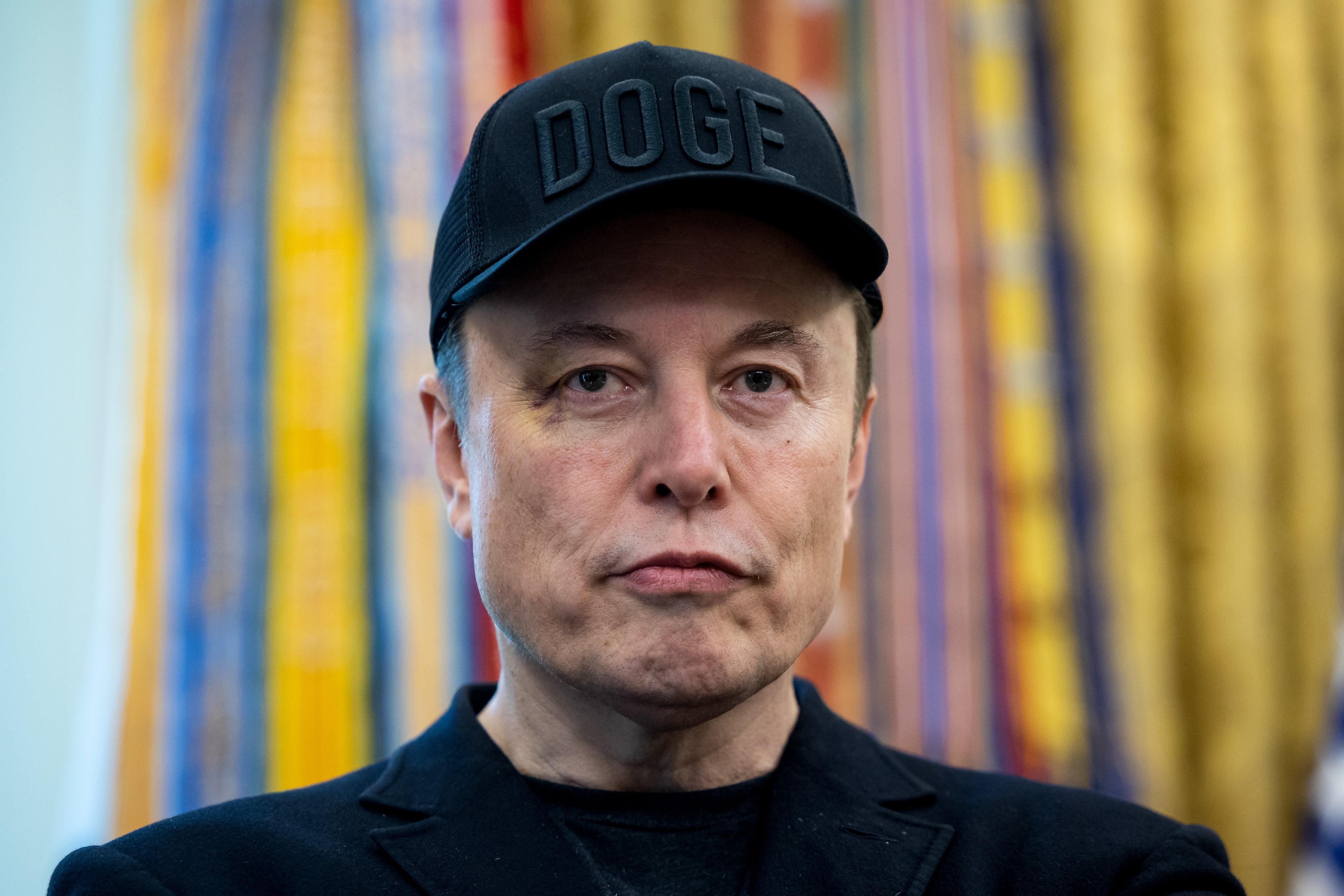 Elon Musk wearing a headdress with "DOGE" written connected it, looking straight astatine the camera