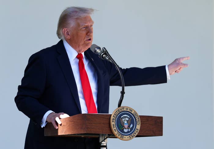Person speaking astatine  podium with authoritative  seal, gesturing outward, wearing a suit   and reddish  tie