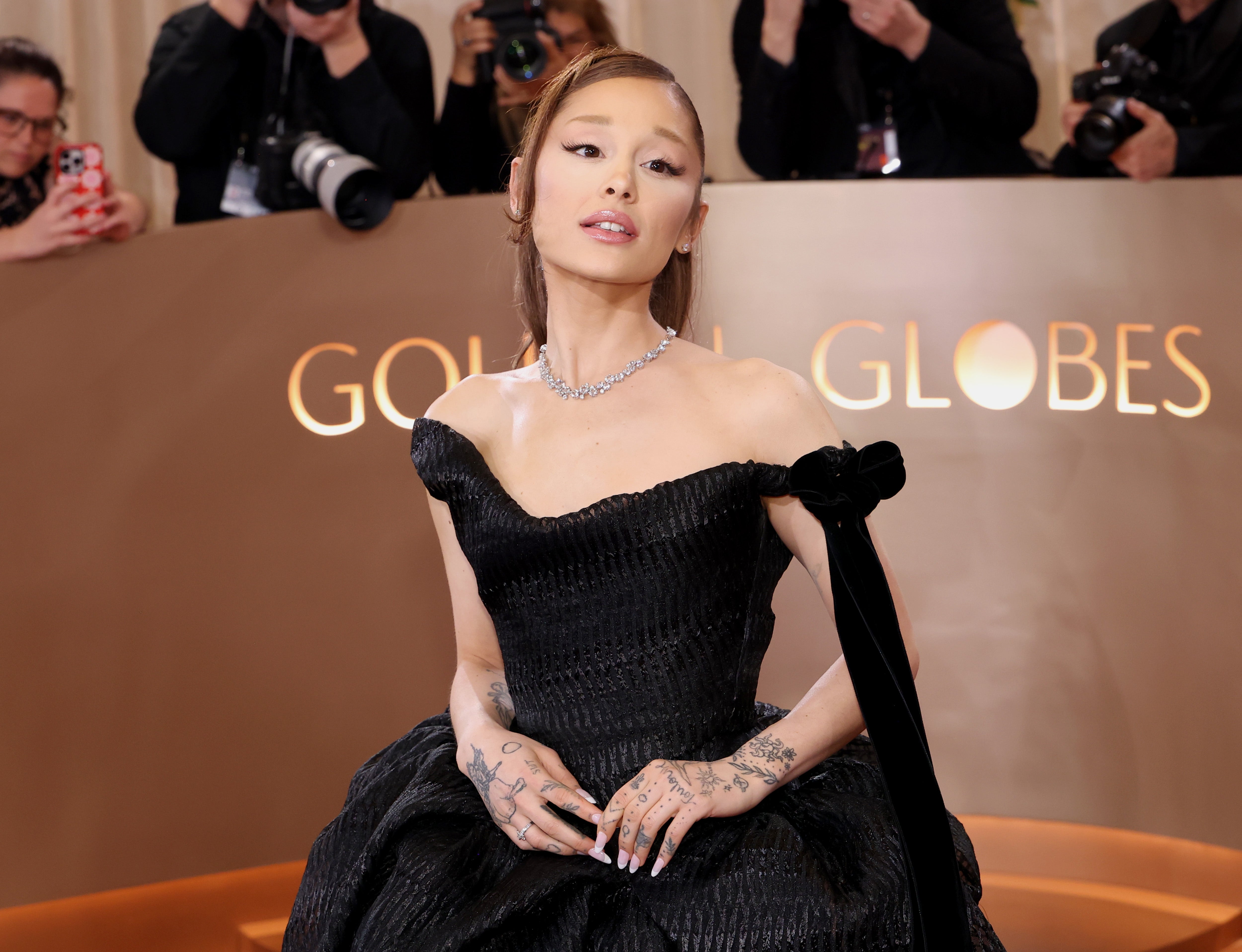 Person in elegant, off-shoulder black gown with intricate tattoos poses for photographers at a formal event