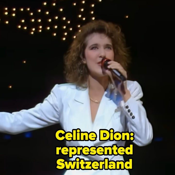 Singer performing on stage in a sleek white suit, holding a microphone with star-like lights in the background