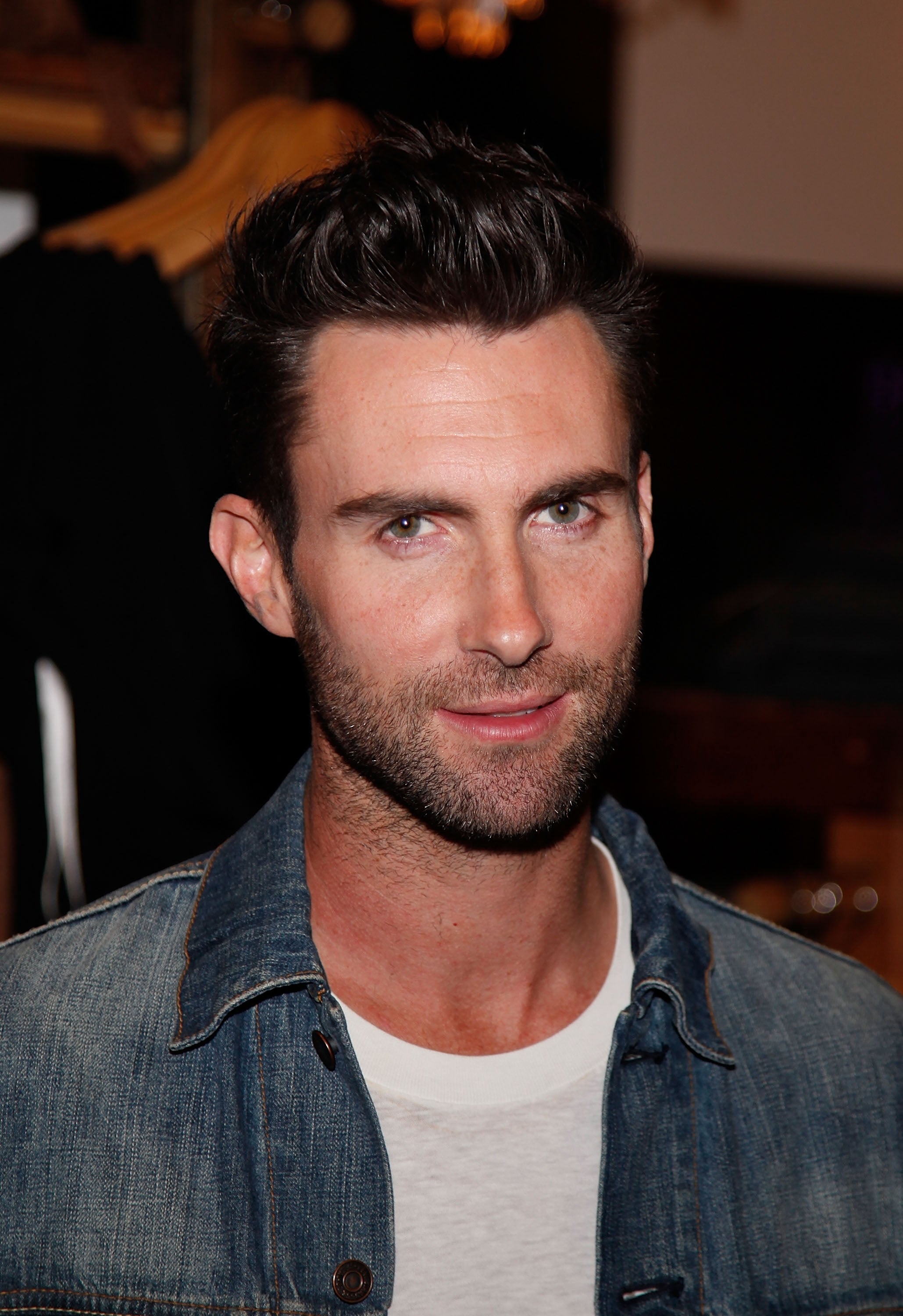 Adam Levine wears a casual white shirt and denim jacket while smiling