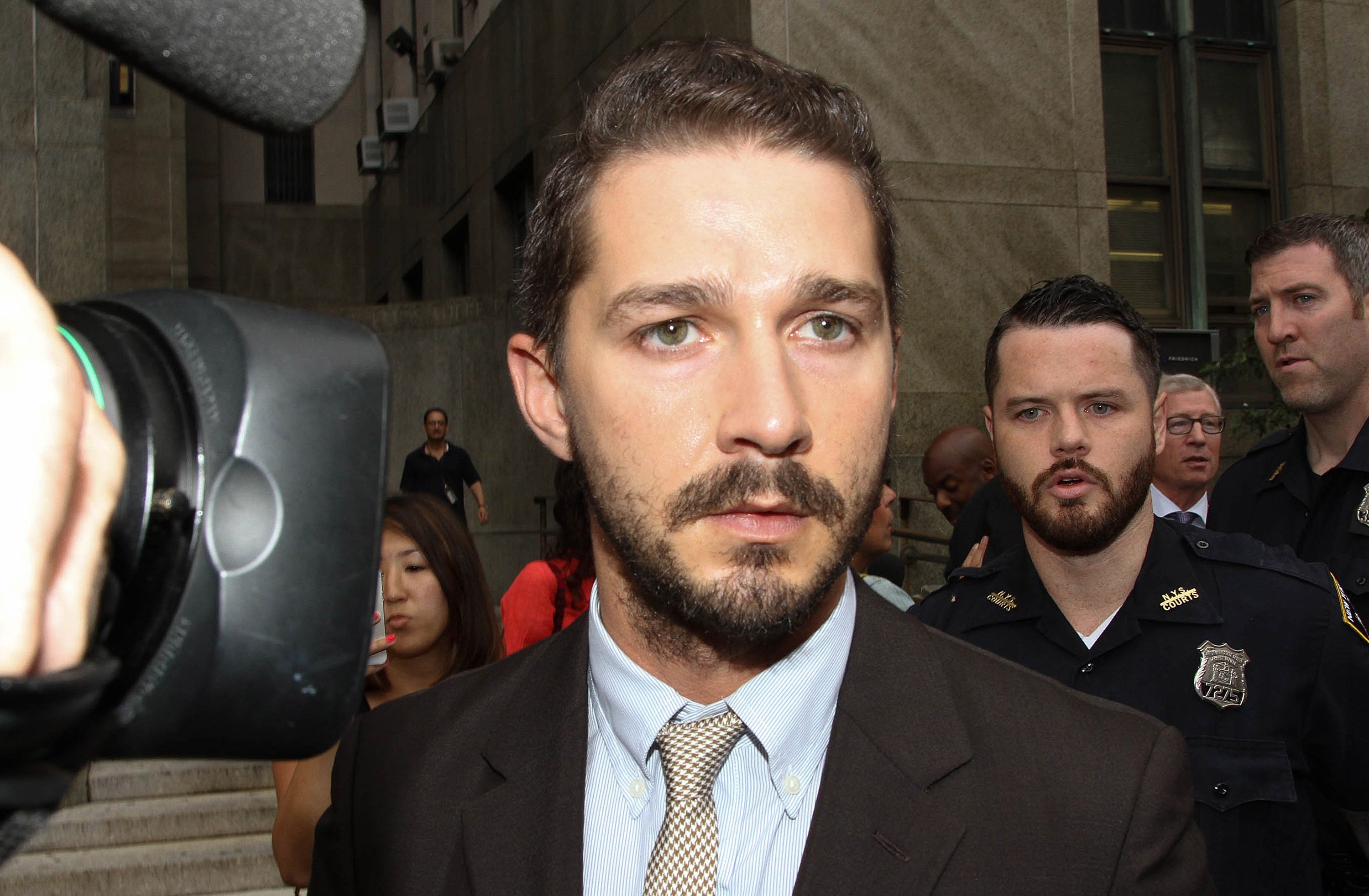 Shia LaBeouf wears a suit and tie and appears serious while being photographed and interviewed