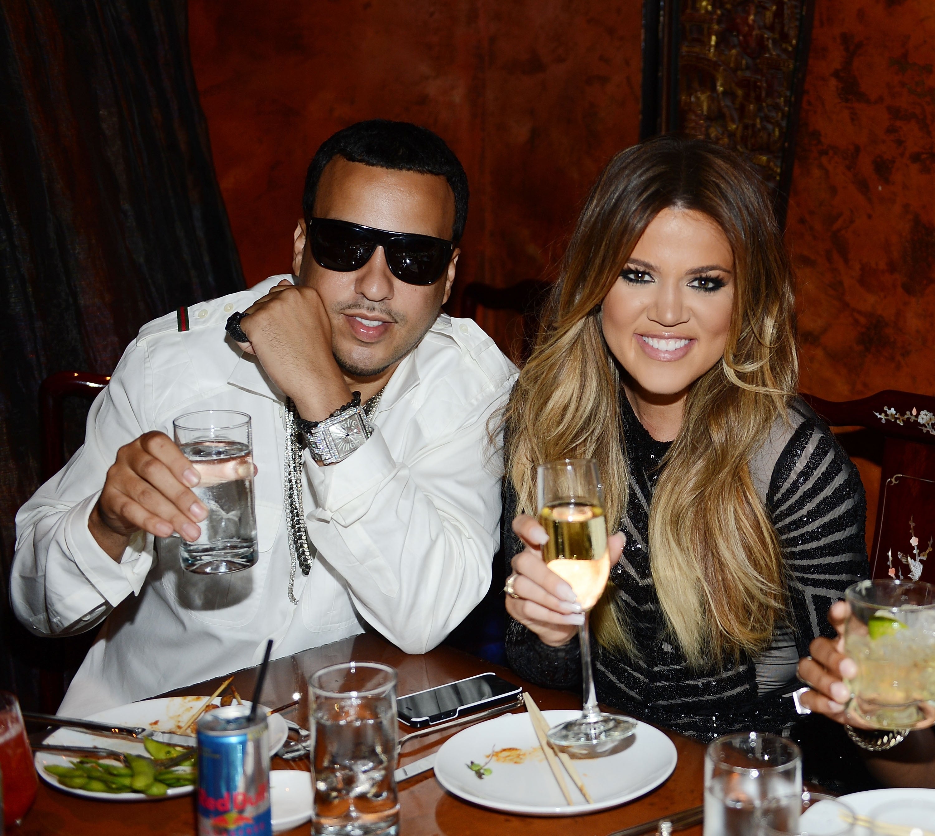 Two people smiling at a dining table, holding drinks. The person on the right is wearing a striped outfit