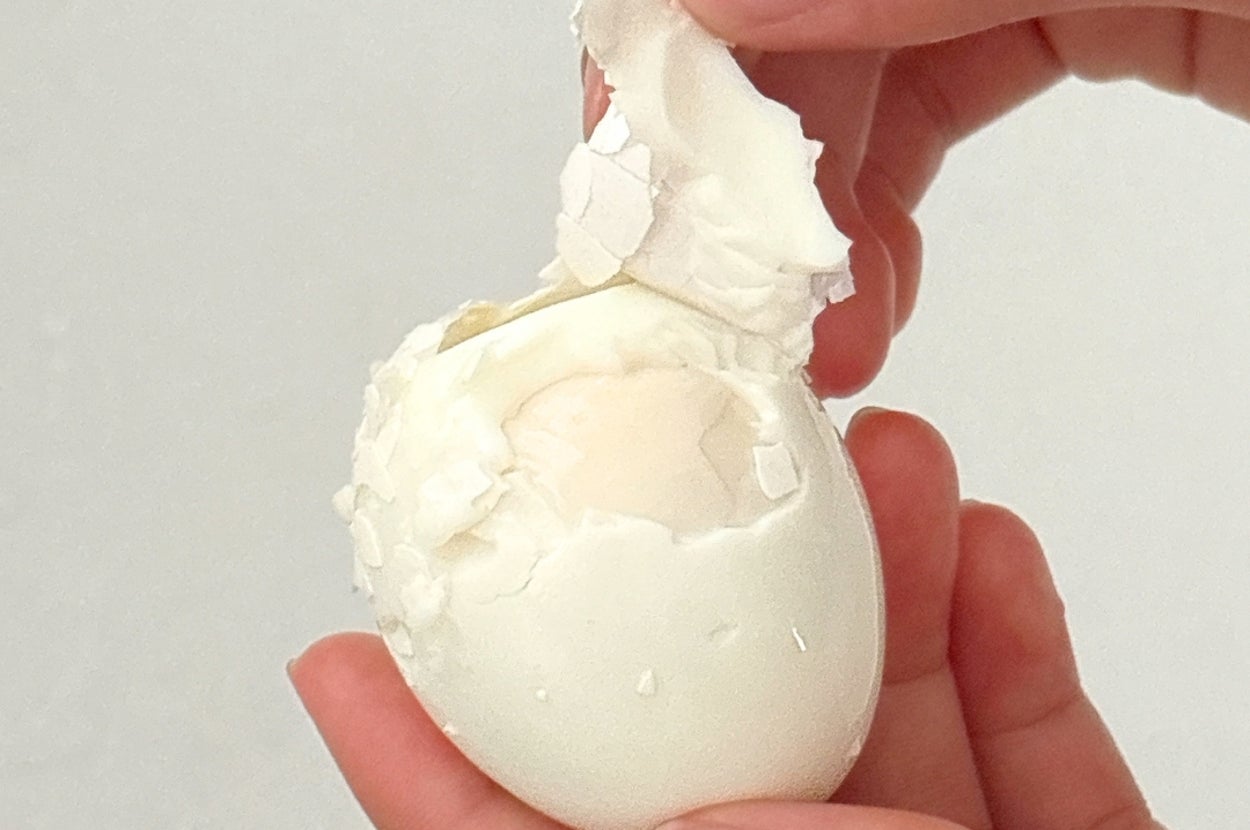 手で殻を剥かれているゆで卵。