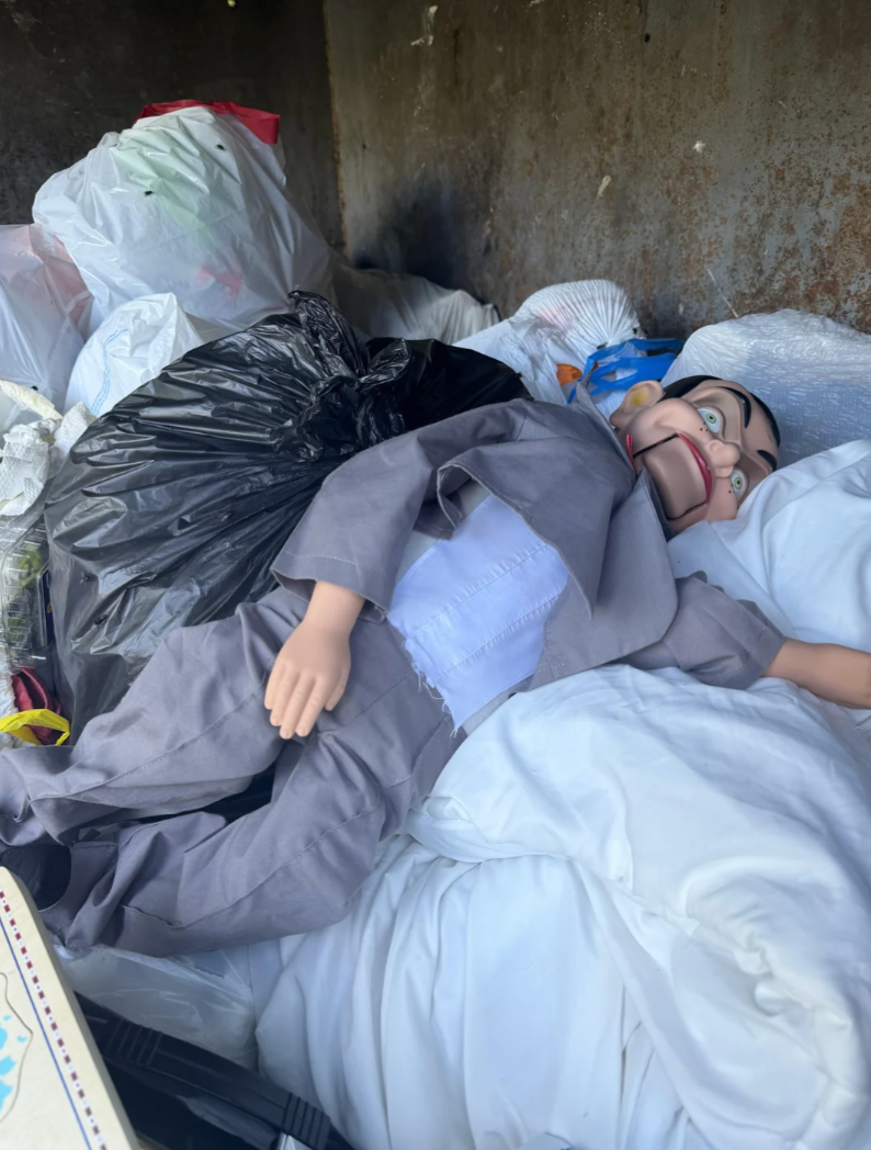 Ventriloquist dummy successful a grey suit lies atop bags of trash successful a dumpster