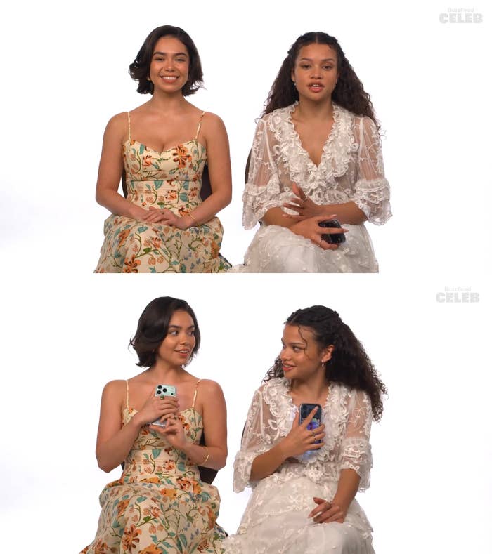 Two smiling women seated, one in a floral dress and the other in a lacy white outfit, holding phones and engaging in a conversation