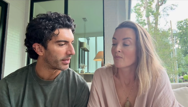 Two people sitting together in a modern home setting, looking at each other attentively. One person is wearing a casual t-shirt, the other a loose top