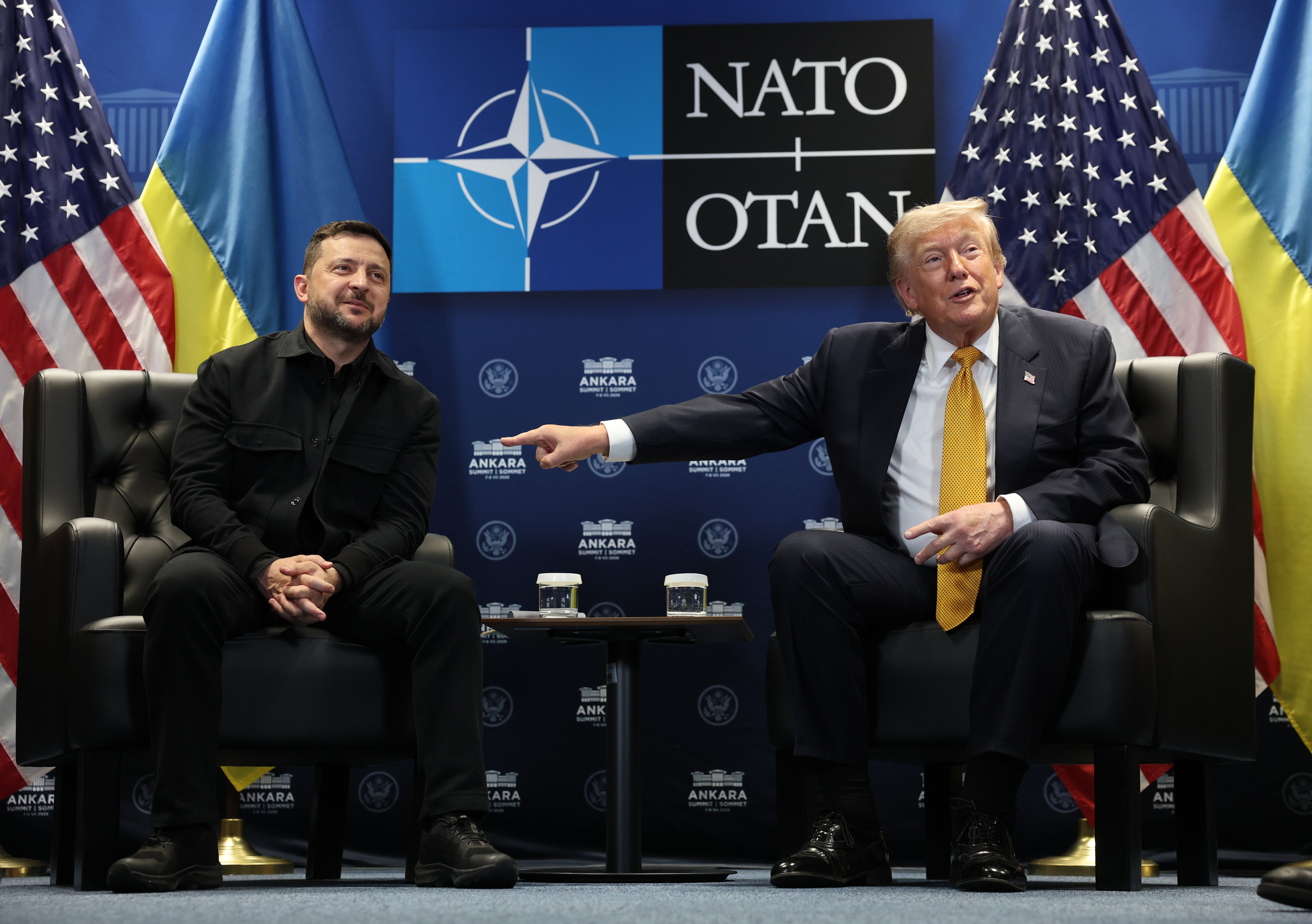 To menn satt ved NATO-bakgrunn, den ene i mørk dress, den andre i dress med et lyst slips, engasjert i samtale