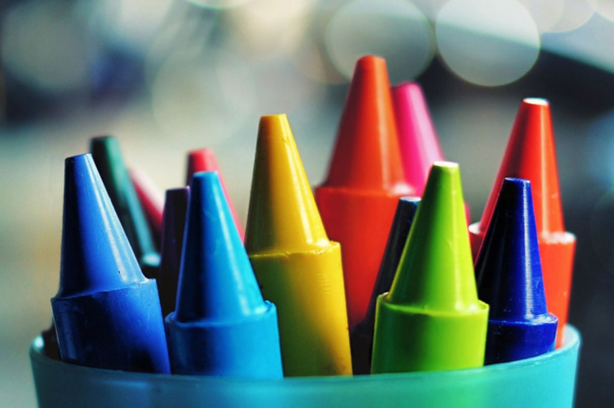 Crayons of various colors, sharpened and standing upright in a holder, with blurred background