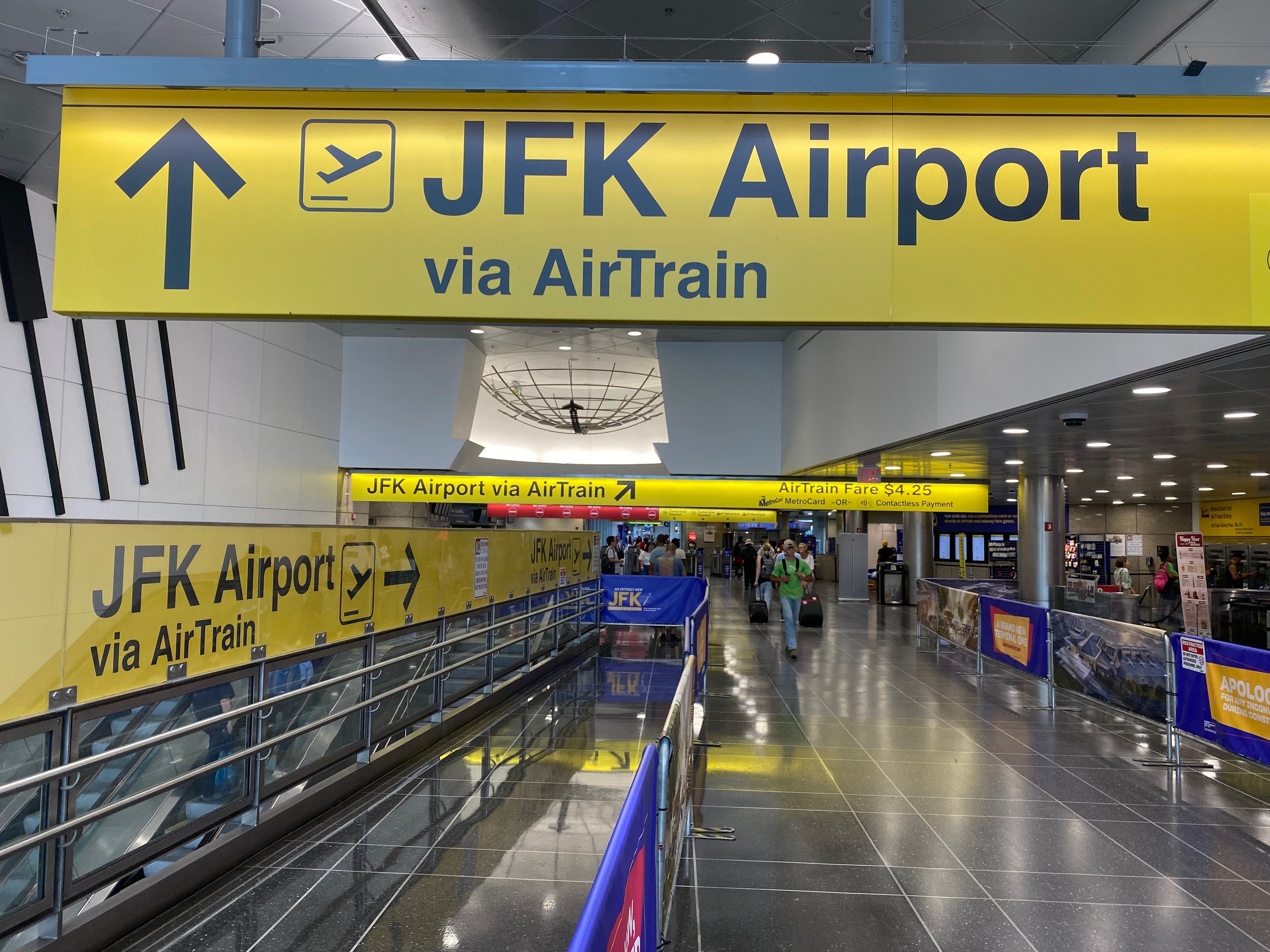 JFK Airport signage directing passengers to use the AirTrain, with people walking along the terminal