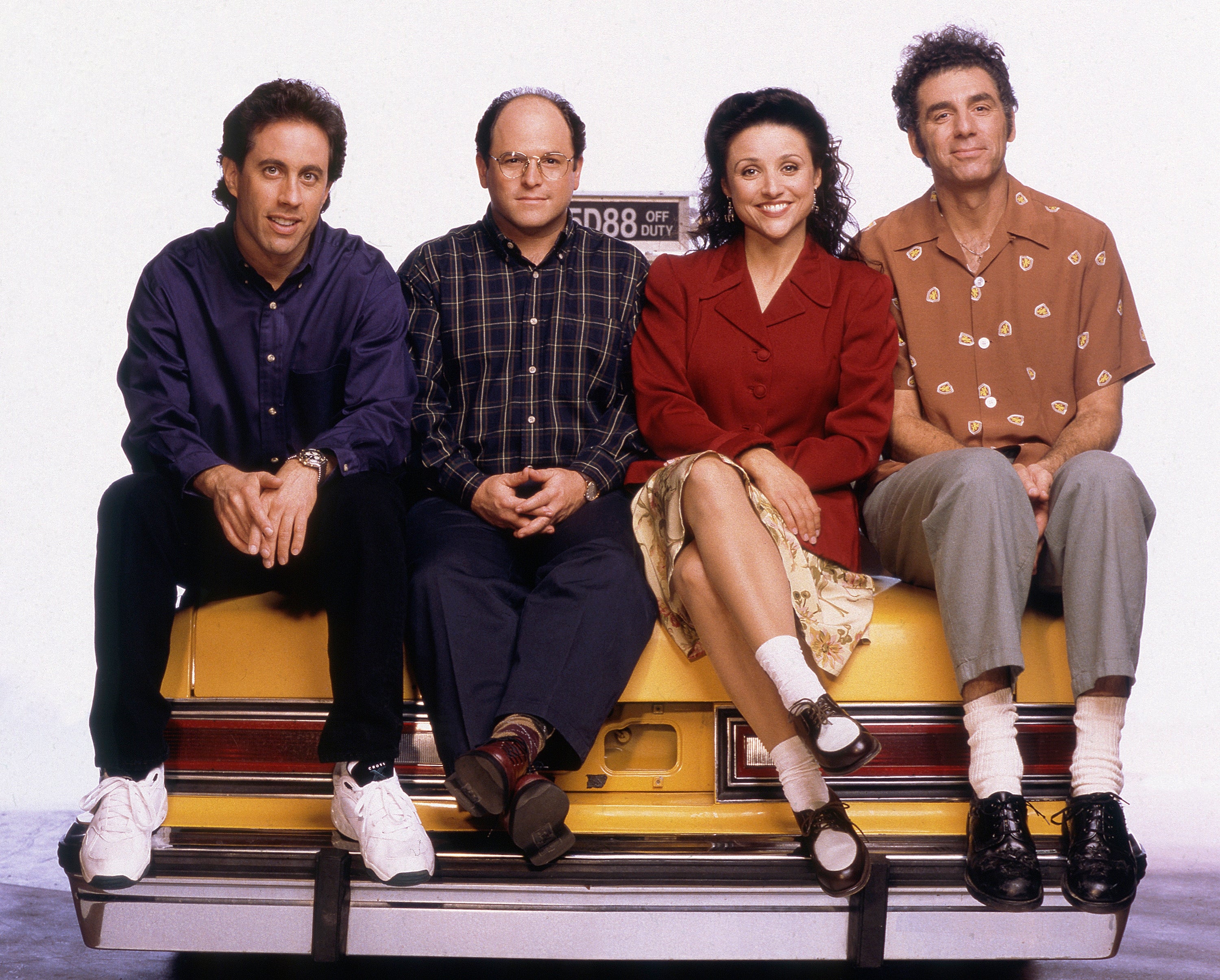 Four people sit on a taxi, posing casually. They wear 90s casual and smart-casual outfits, including button-up shirts and sneakers