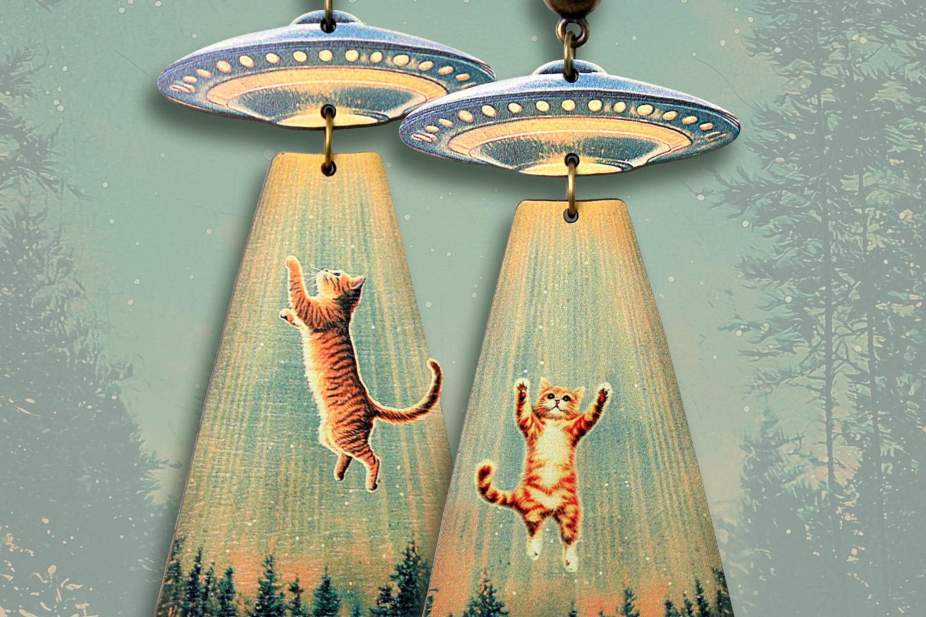 Earrings featuring UFOs beaming up playful cats in a whimsical forest scene