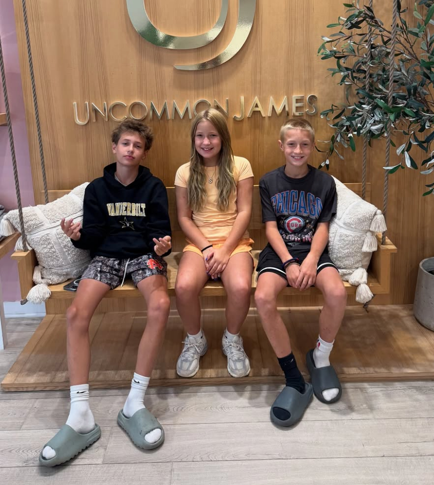 Three children sit on a swing inside Uncommon James, smiling at the camera