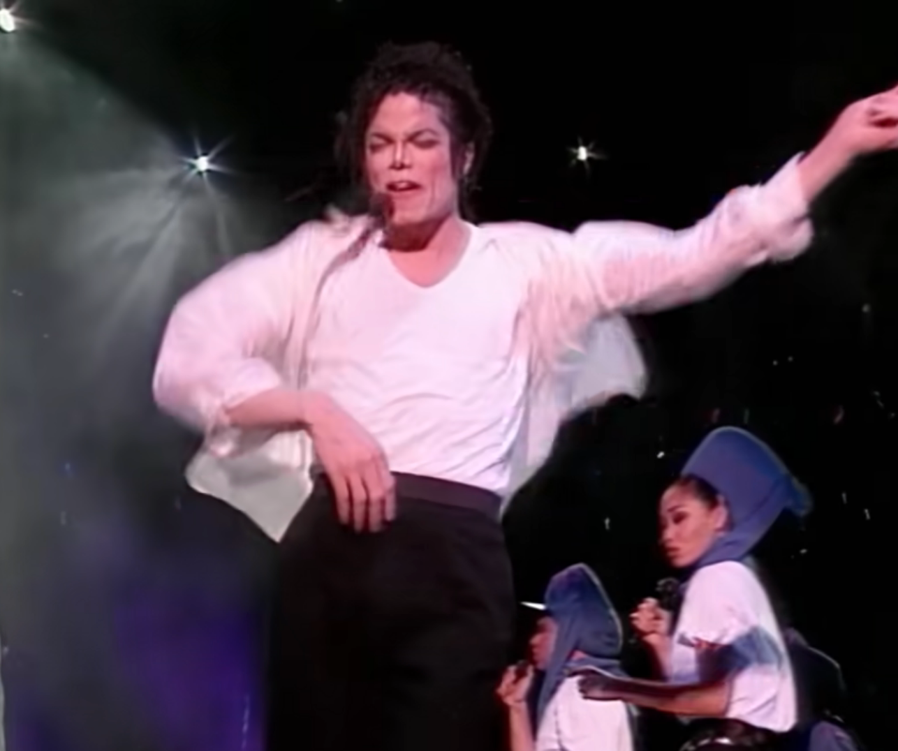 Performer energetically dances on stage with backup dancers in matching outfits during a concert