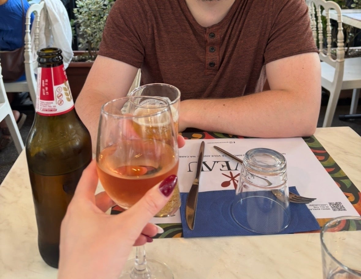 Two people toast with drinks at an outdoor café table set with menus and utensils. A relaxed and casual dining experience