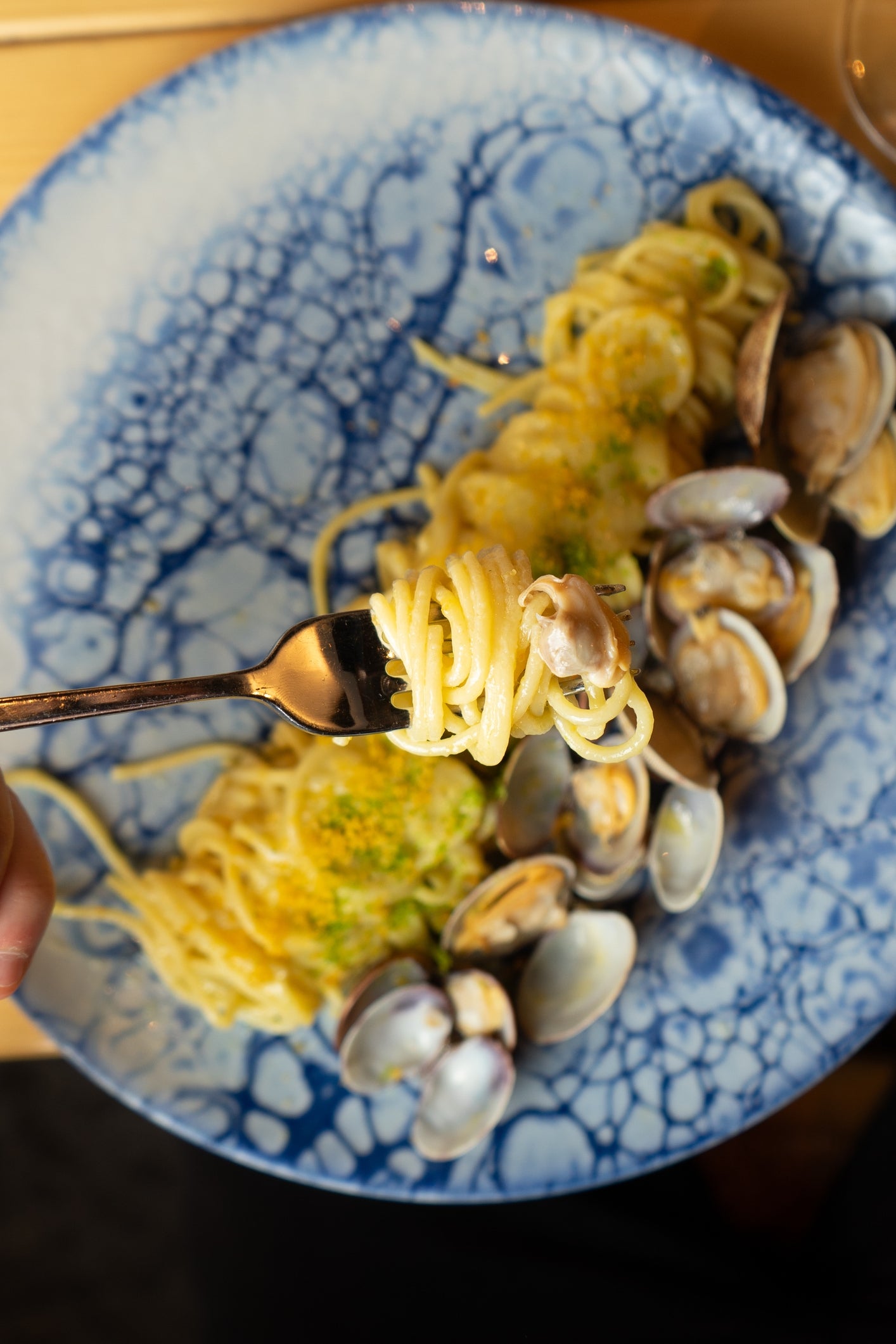 A fork twirls spaghetti with clams on a textured blue plate, suggesting a seafood meal experience