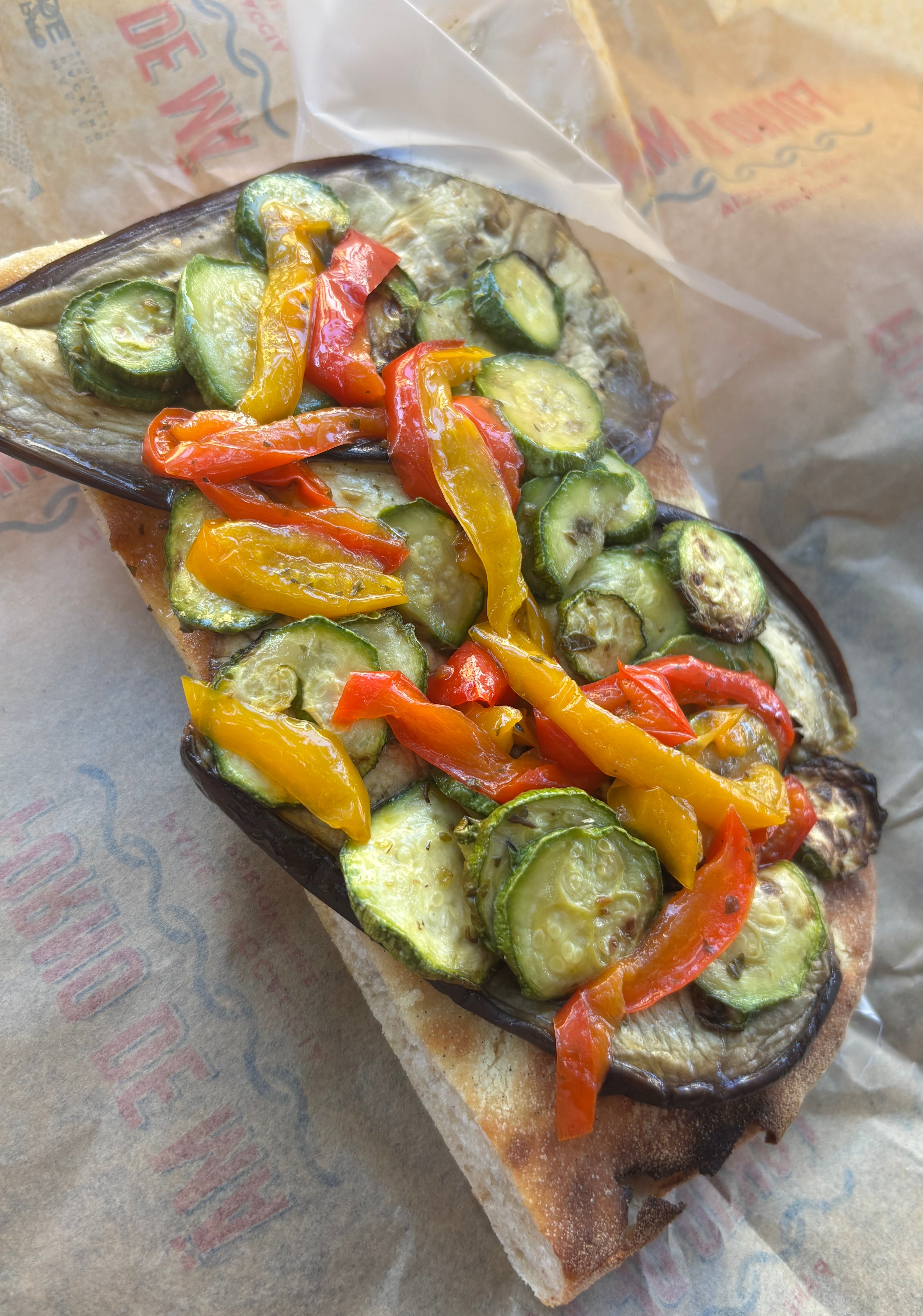 Open-faced sandwich topped with sliced zucchini, eggplant, and red peppers on parchment paper