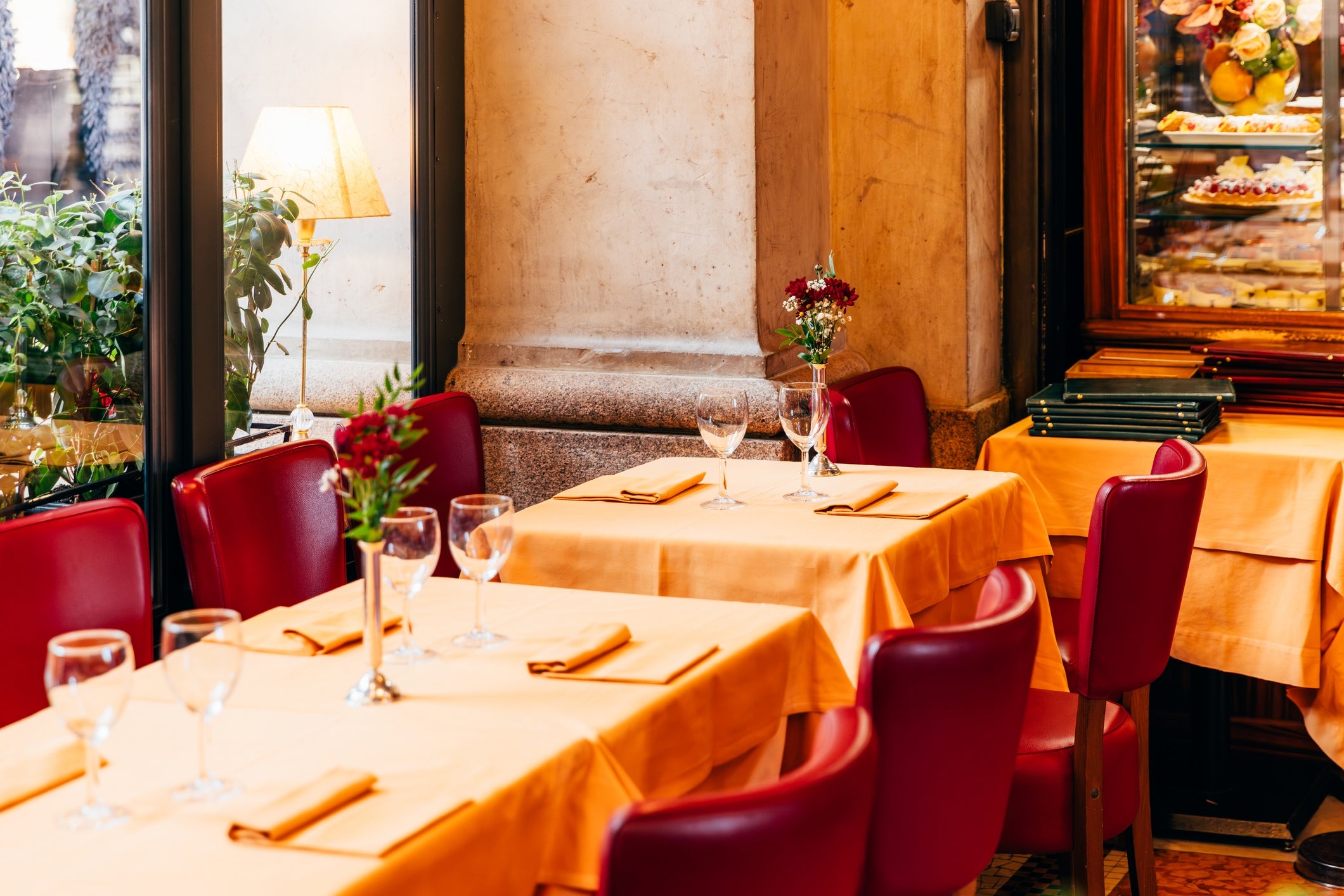 Cozy restaurant setting with red chairs and elegantly set tables by large windows, evoking a warm and inviting dining atmosphere