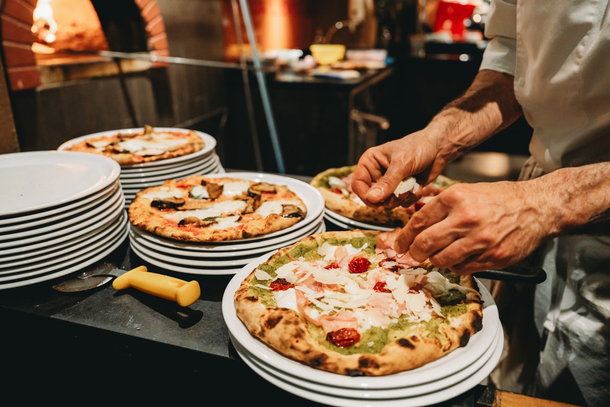 Chef preparing gourmet pizzas in a rustic kitchen, with plates stacked nearby