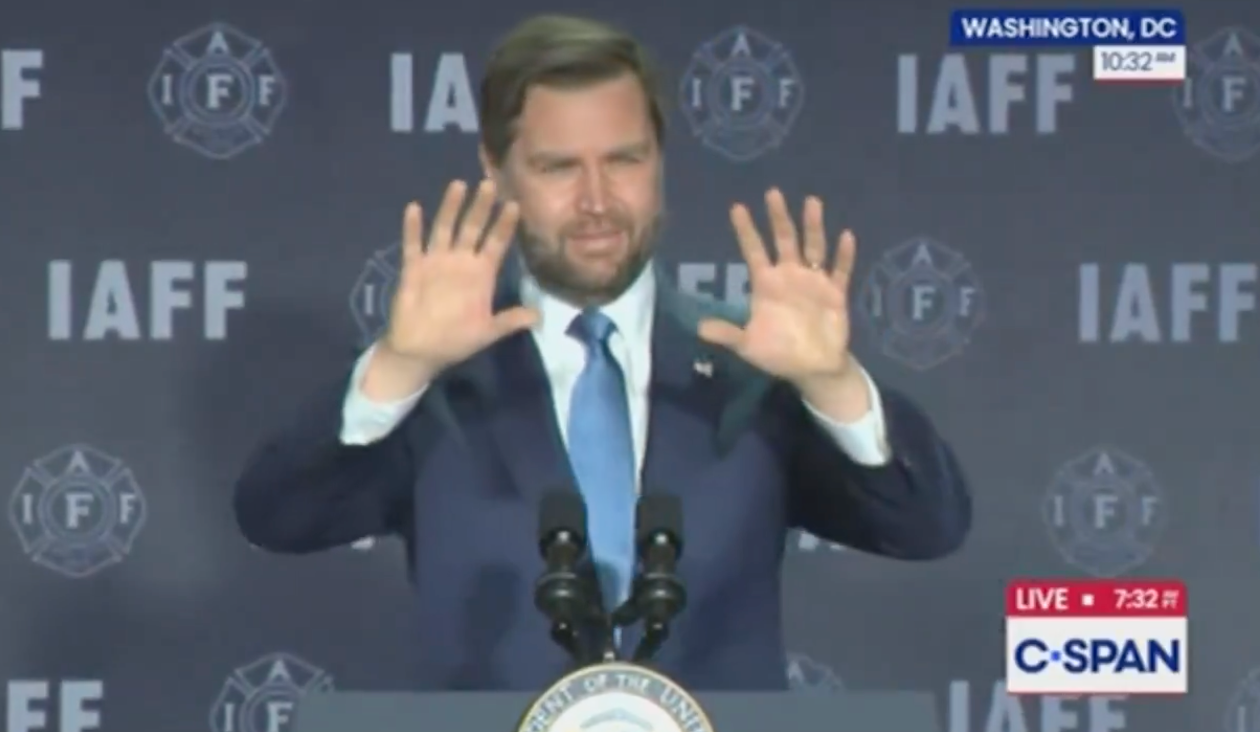 En mann i dress snakker på et podium med «IAFF»; i bakgrunnen og løfter hendene. C-SPAN og Washington, DC tekst vises på skjermen