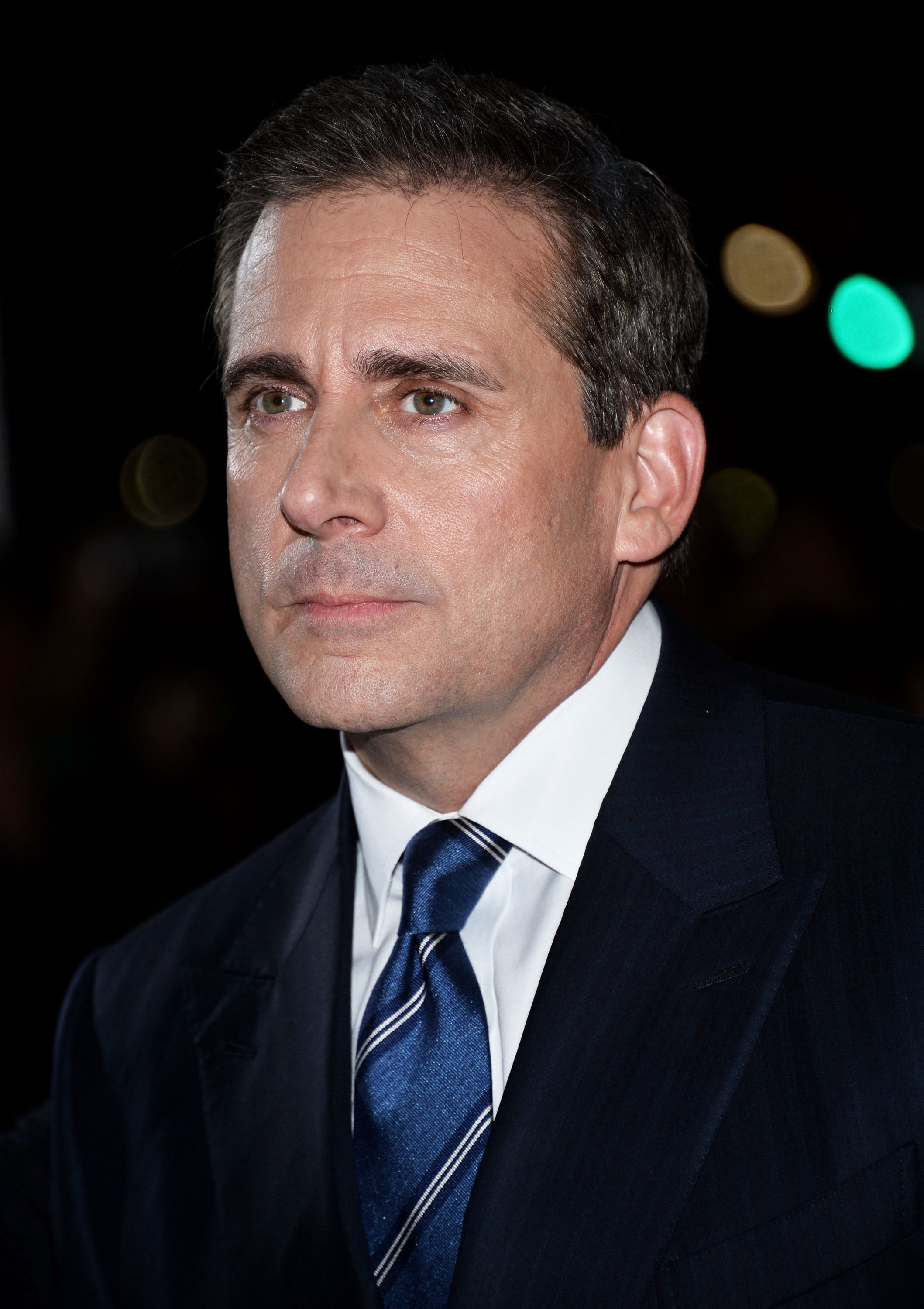 Steve Carell wears a suit with a blue tie. He looks pensive and serious