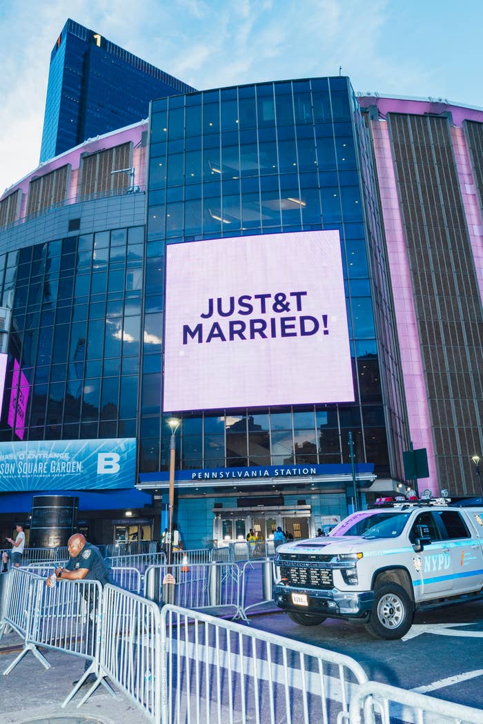 Billboard outside Pennsylvania Station reads "JUST MARRIED!" above a bustling street, with police presence visible