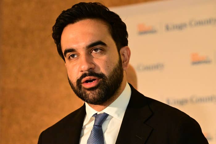 A person in a suit and tie speaks at a podium at an event, with a branded backdrop