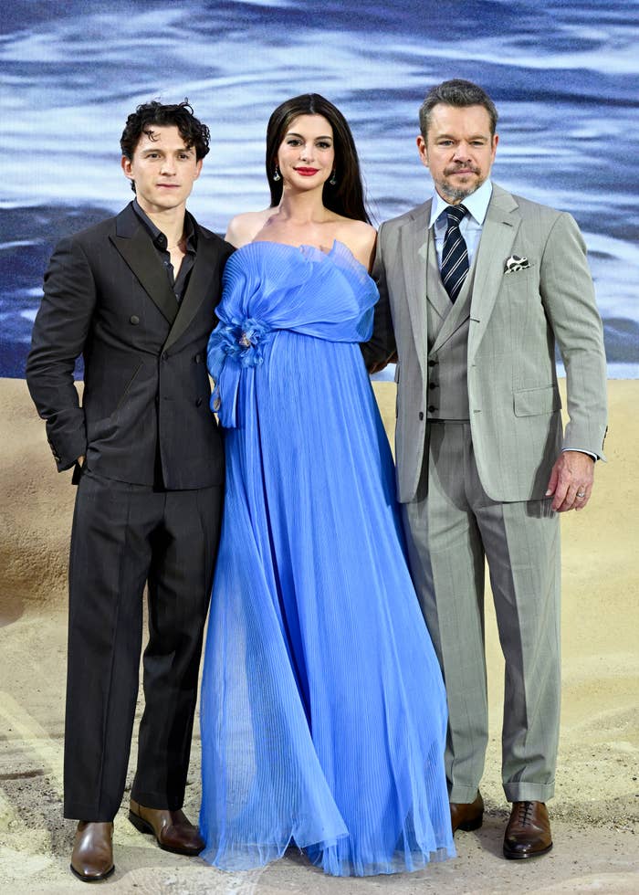  one in a black suit, one in a flowing gown, and one in a gray suit. They are posing for the cameras