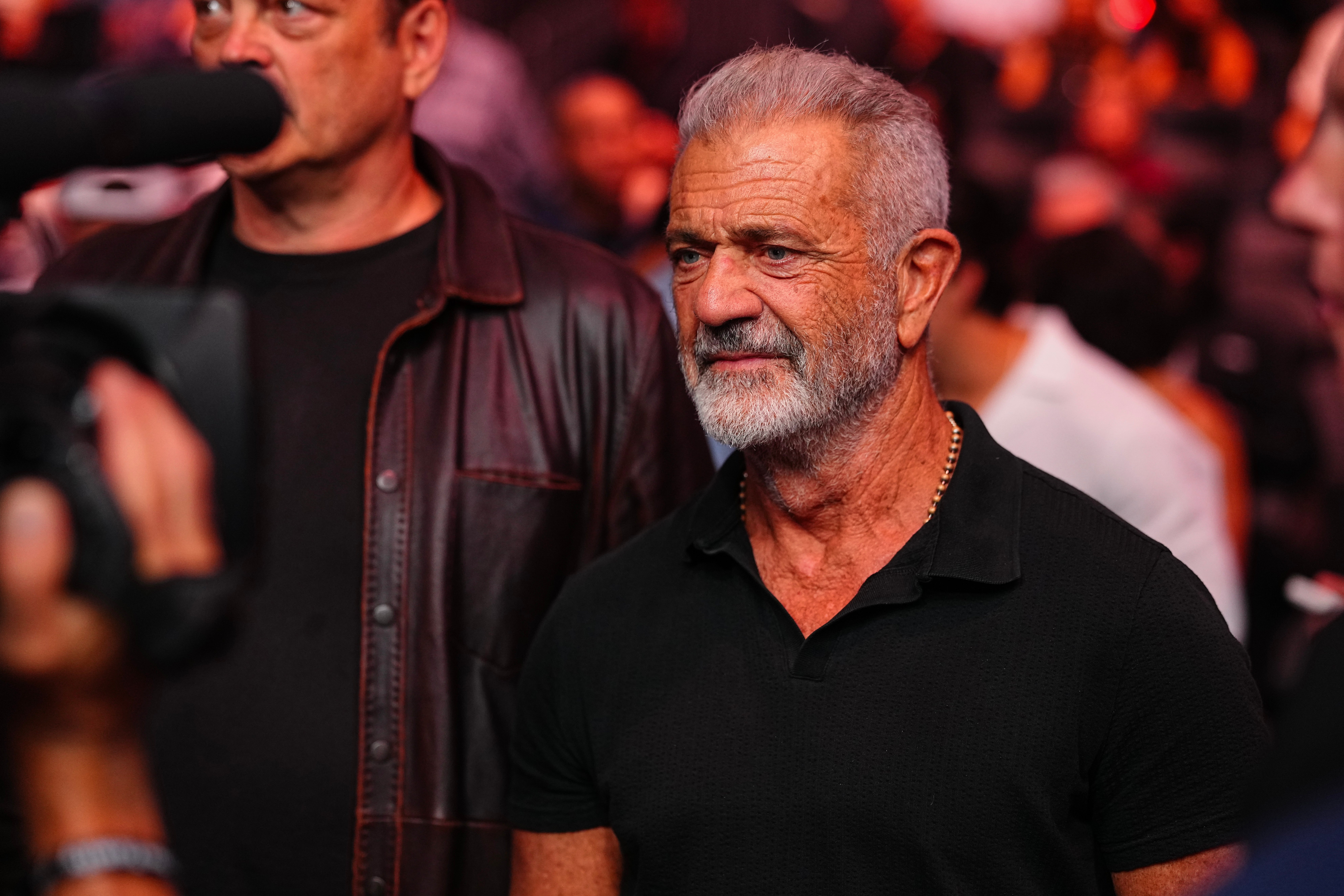 Mel Gibson  with a beard in a polo shirt is at a crowded event, captured in a candid moment