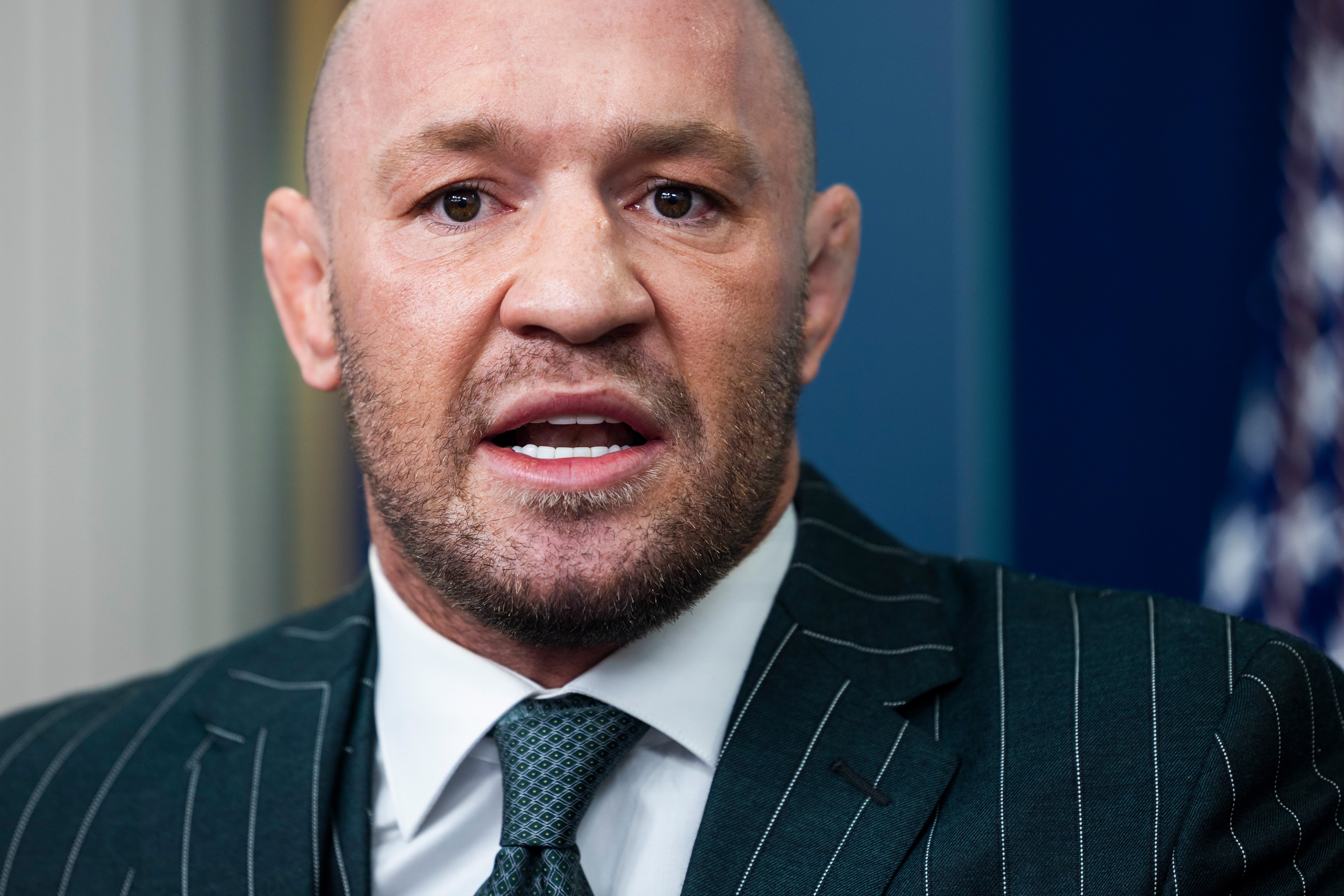Conor McGregor in a pinstripe suit and tie speaks, appearing serious and focused in a professional setting