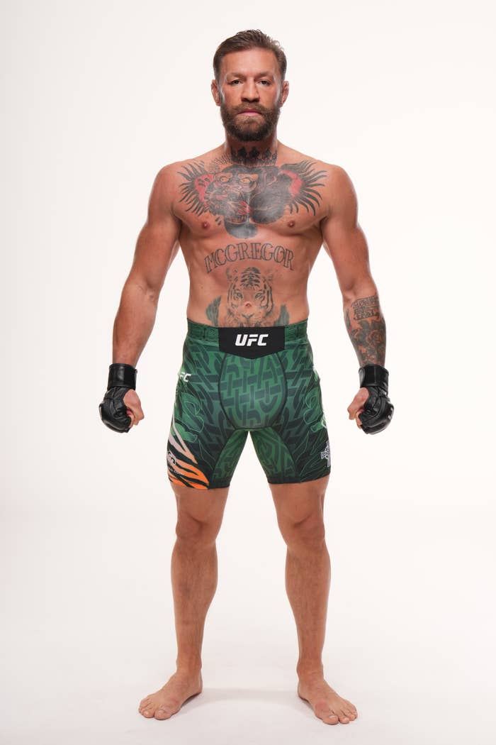 Conor McGregor in patterned shorts and gloves, showcasing multiple tattoos, stands in a confident pose