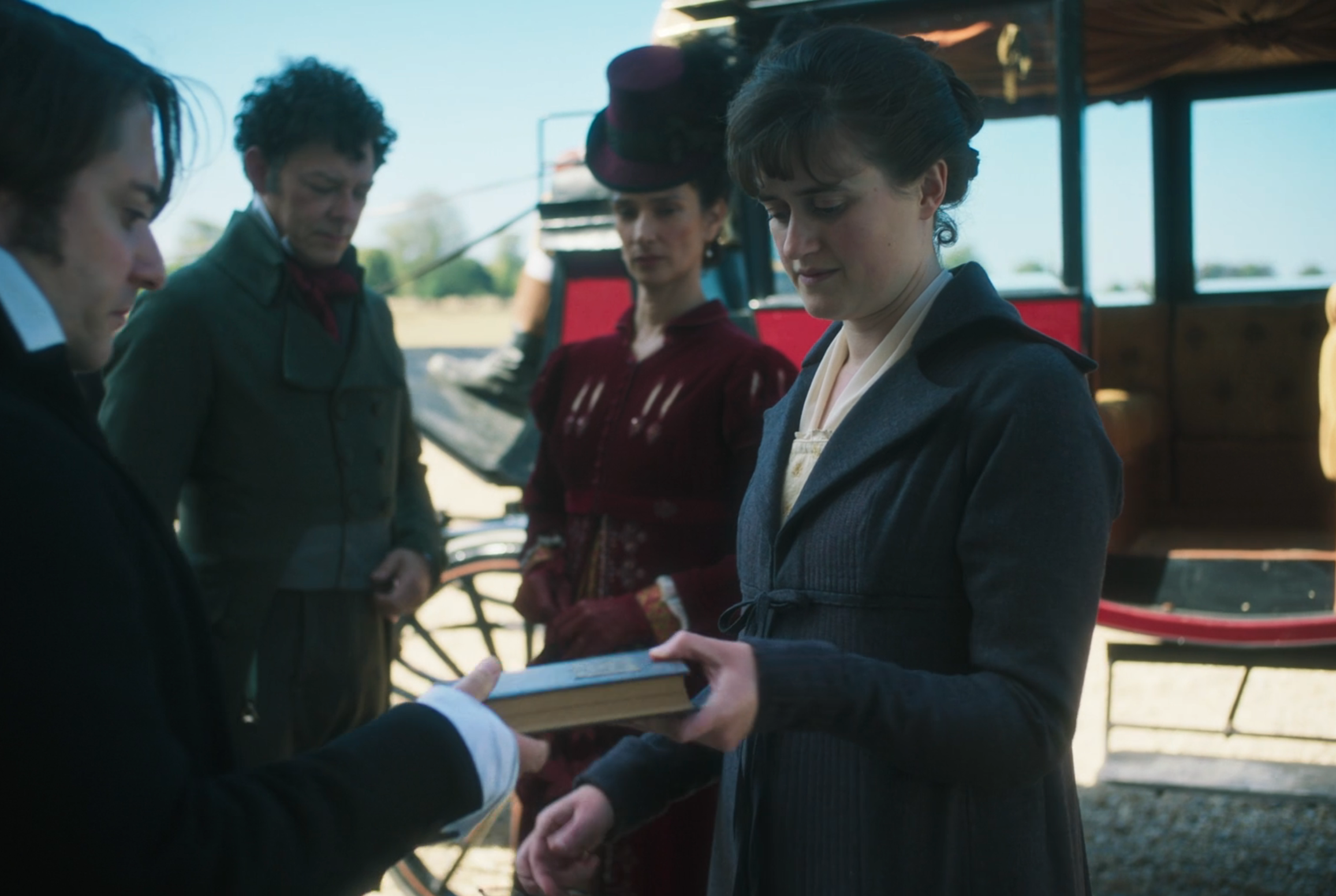 People in 19th-century attire are near a carriage. One woman, in a bonnet, receives a book from a man. Another man and woman look on