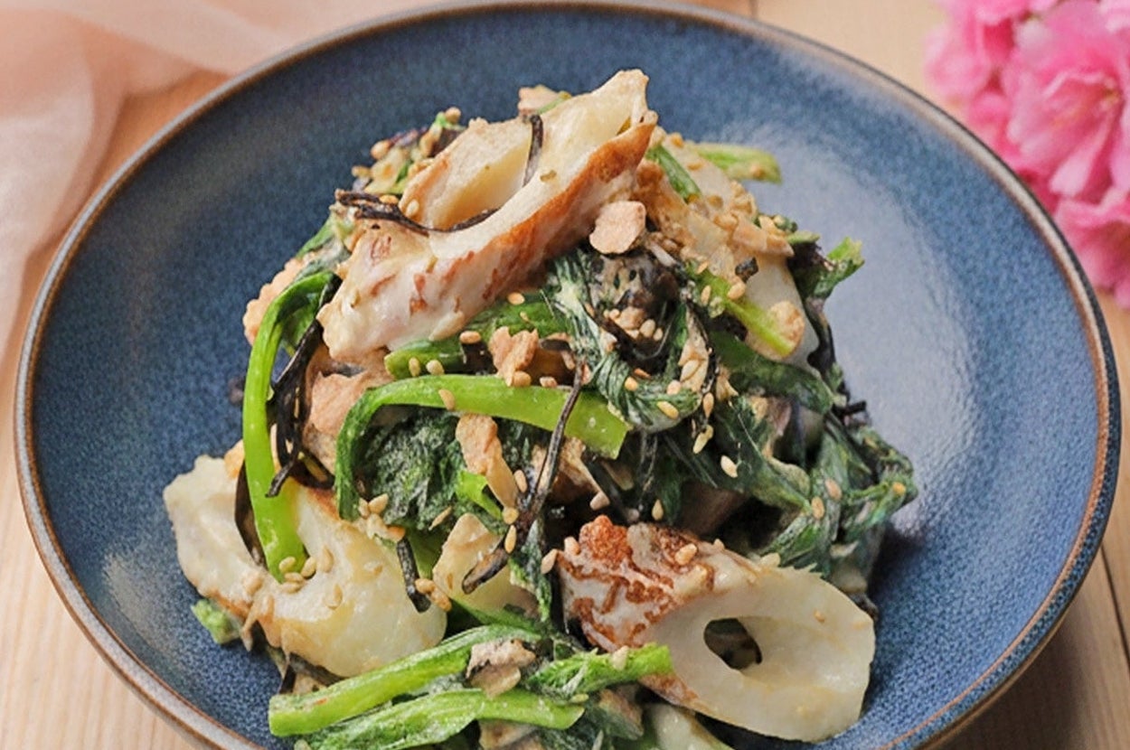 日本料理の盛り付け。ゴマがかかったちくわと野菜のサラダ。木製のテーブルに青い器で提供。