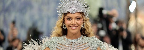 A person in an ornate outfit with feathered details and an elaborate headdress poses confidently at a formal event