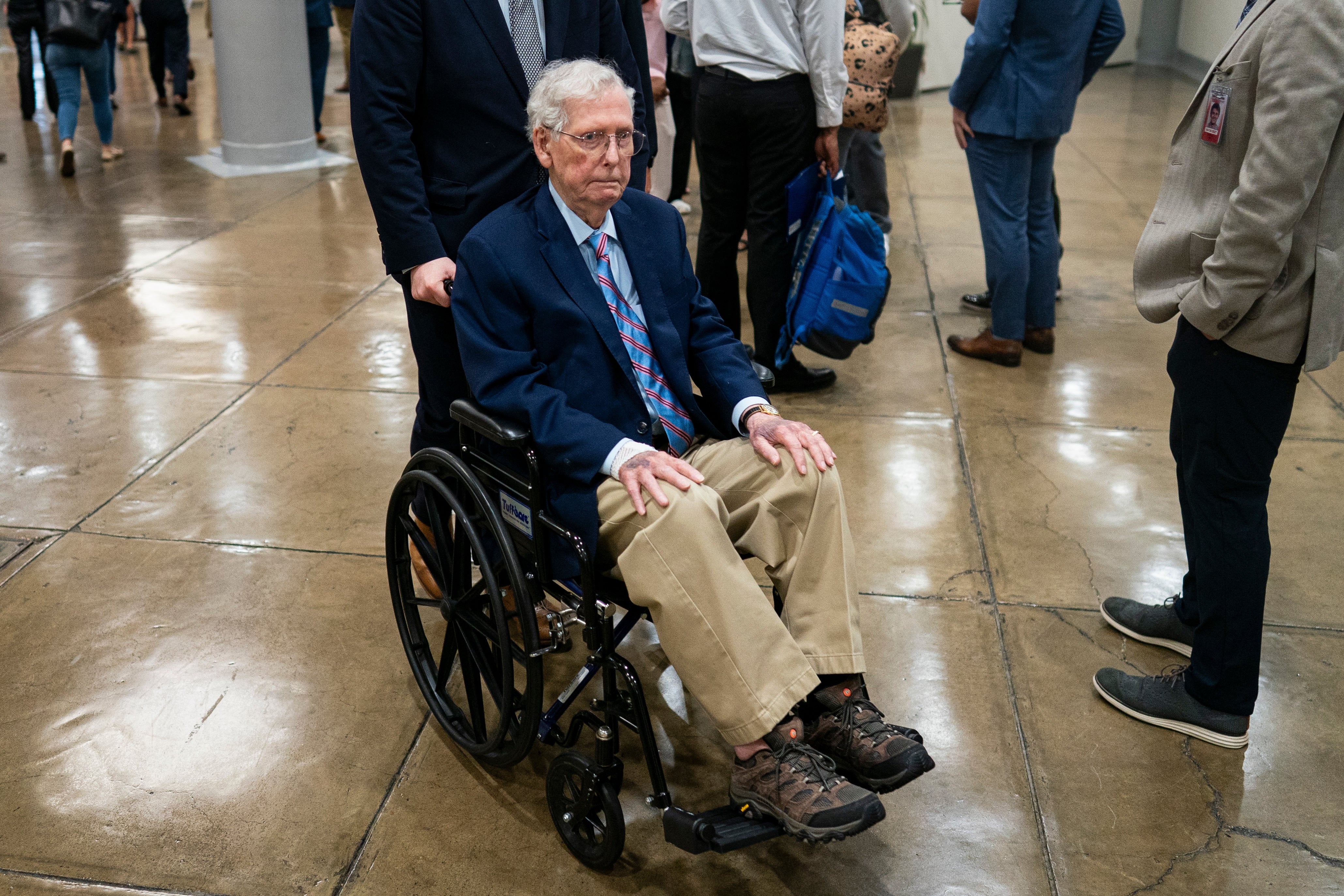 A man in a wheelchair wearing a suit and tie, surrounded by people in a public indoor setting