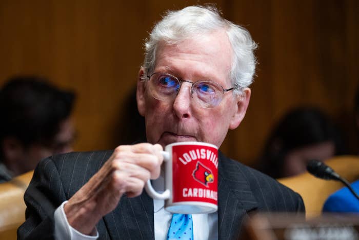 A person in a suit drinks from a "Louisville Cardinals" mug during a formal event