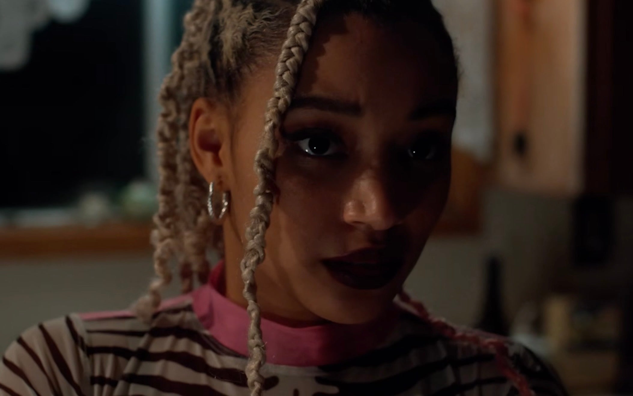 Amandla  with braided hairstyle in a patterned top, looking thoughtfully in a dimly lit setting