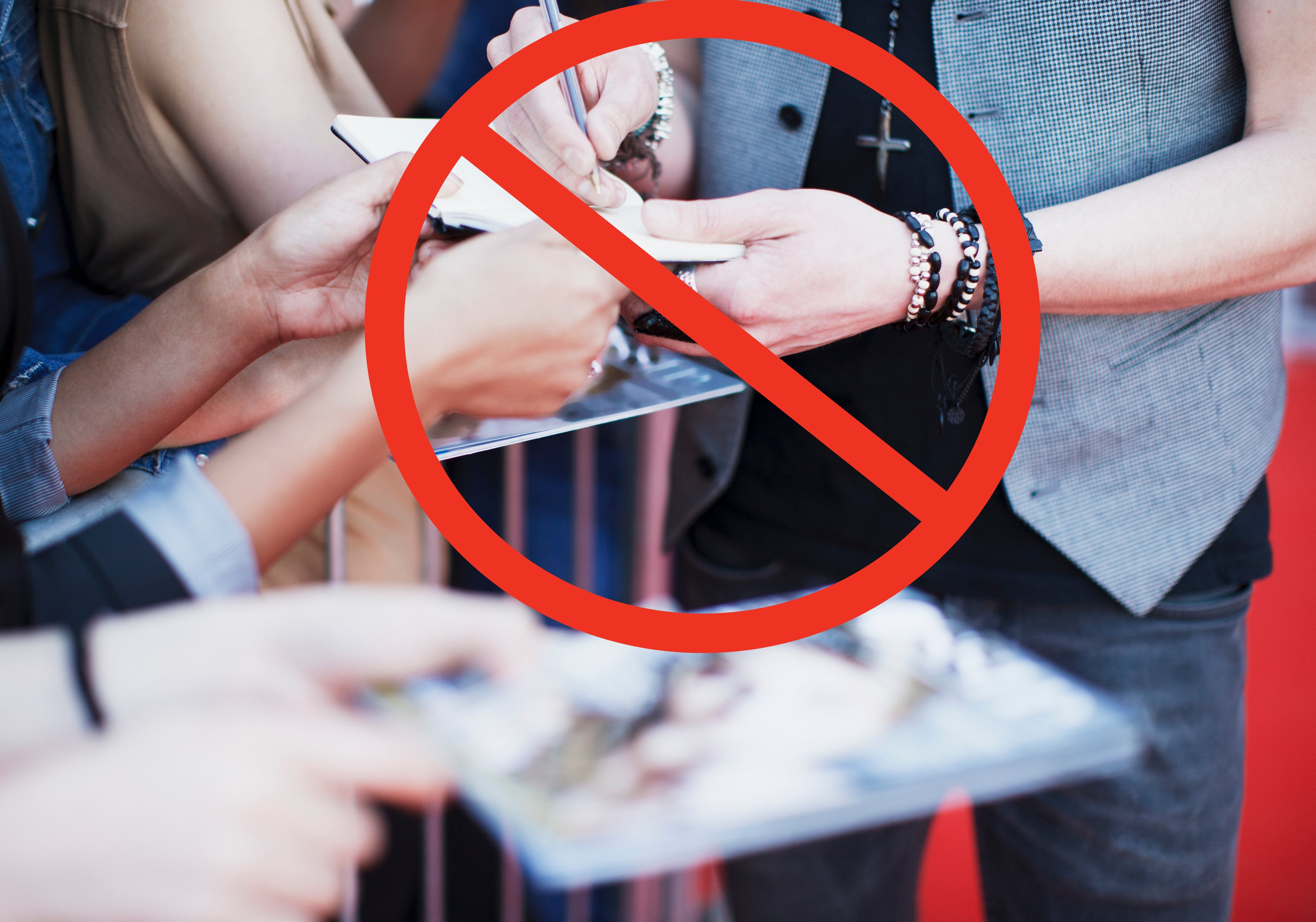 Person in a sleeveless vest signing autographs for fans over a red carpet barrier