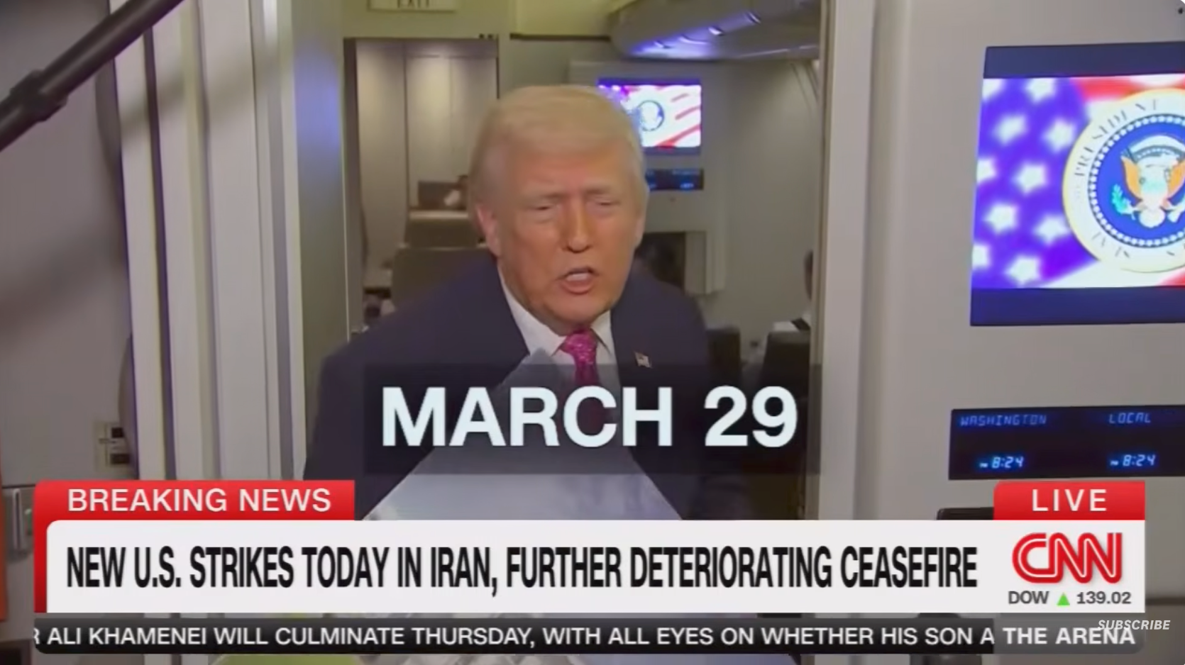 A man in a suit speaks to the camera on a plane; the screen shows breaking news about U.S. strikes in Iran