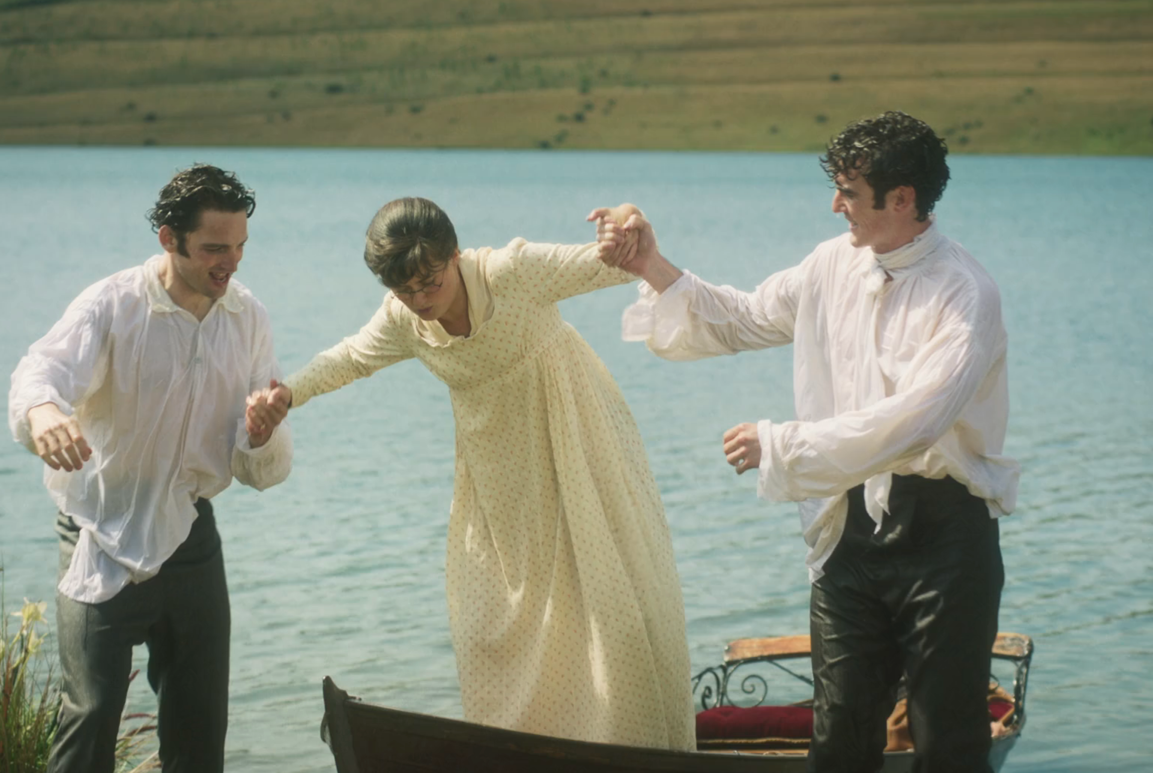 Three people in period-style clothing help each other while getting out of a small boat on a lakeshore