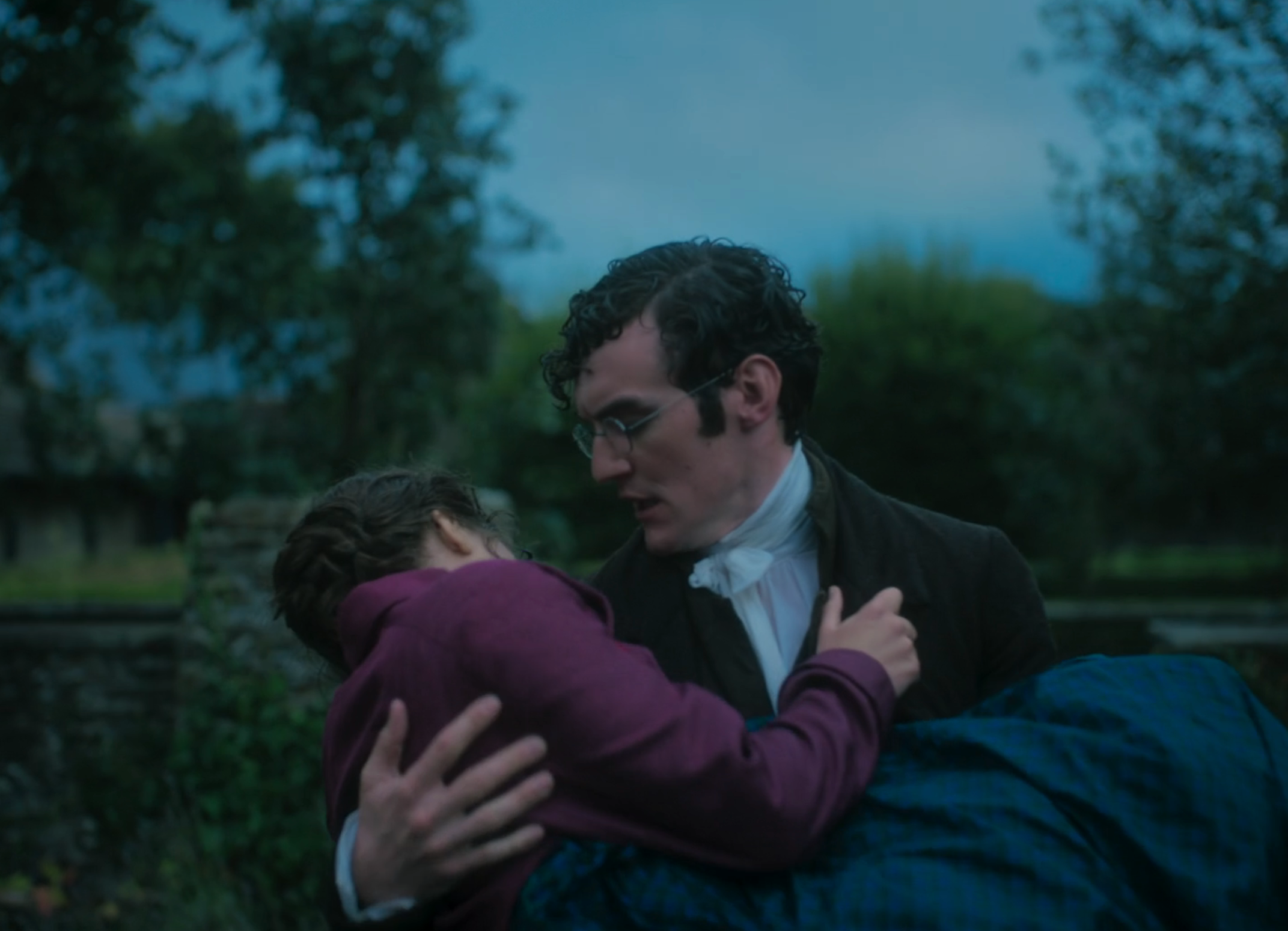 A man in period attire carries a woman in a countryside setting, both appearing distressed