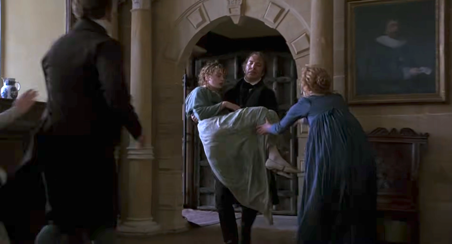 A man carries an unconscious woman in a historical setting, with two people nearby in period clothing, expressing concern