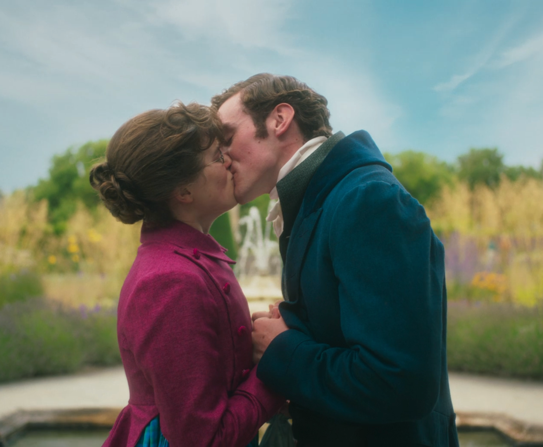 A couple in period costumes shares a kiss in a garden setting