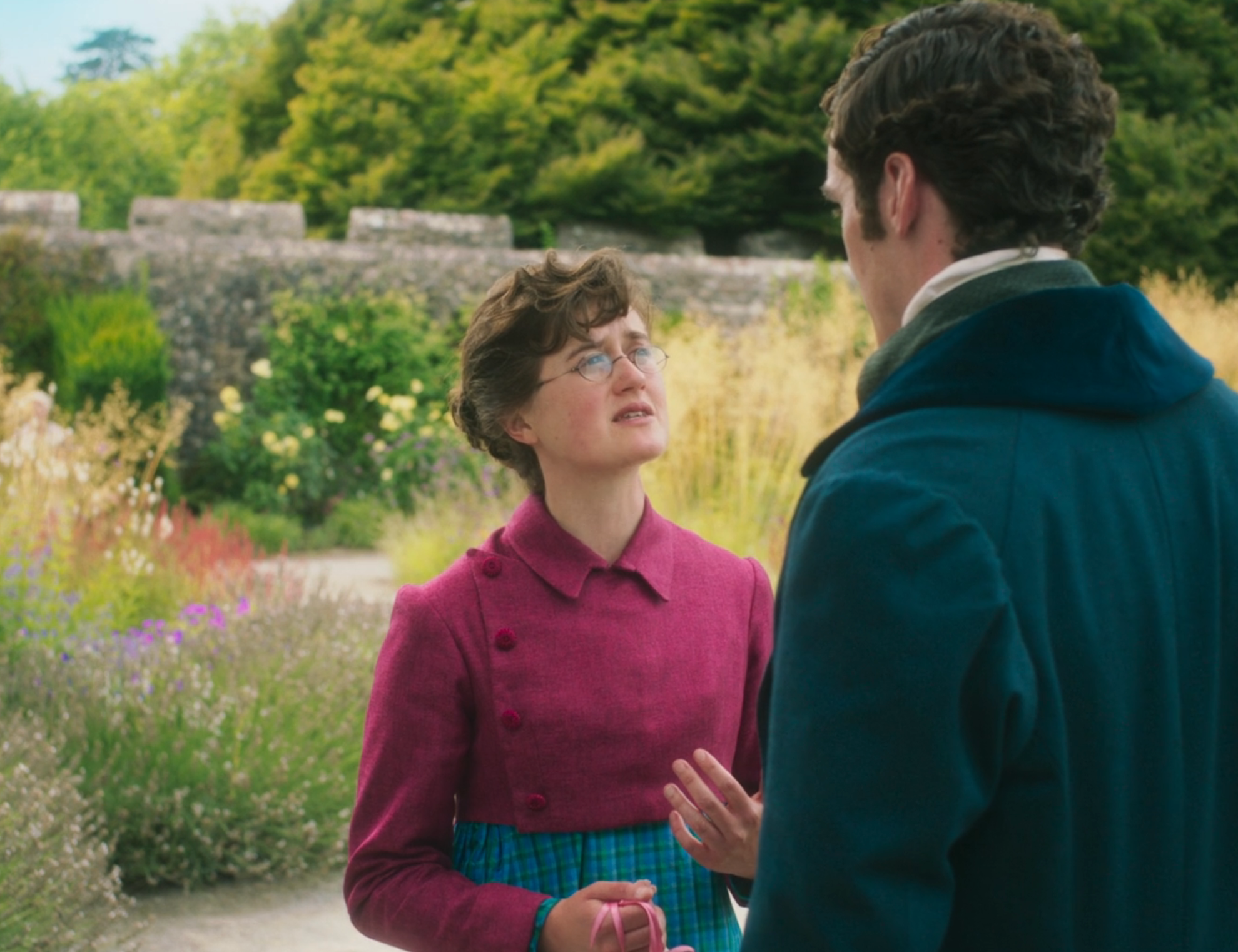 Two people in period clothing have a conversation in a lush garden setting