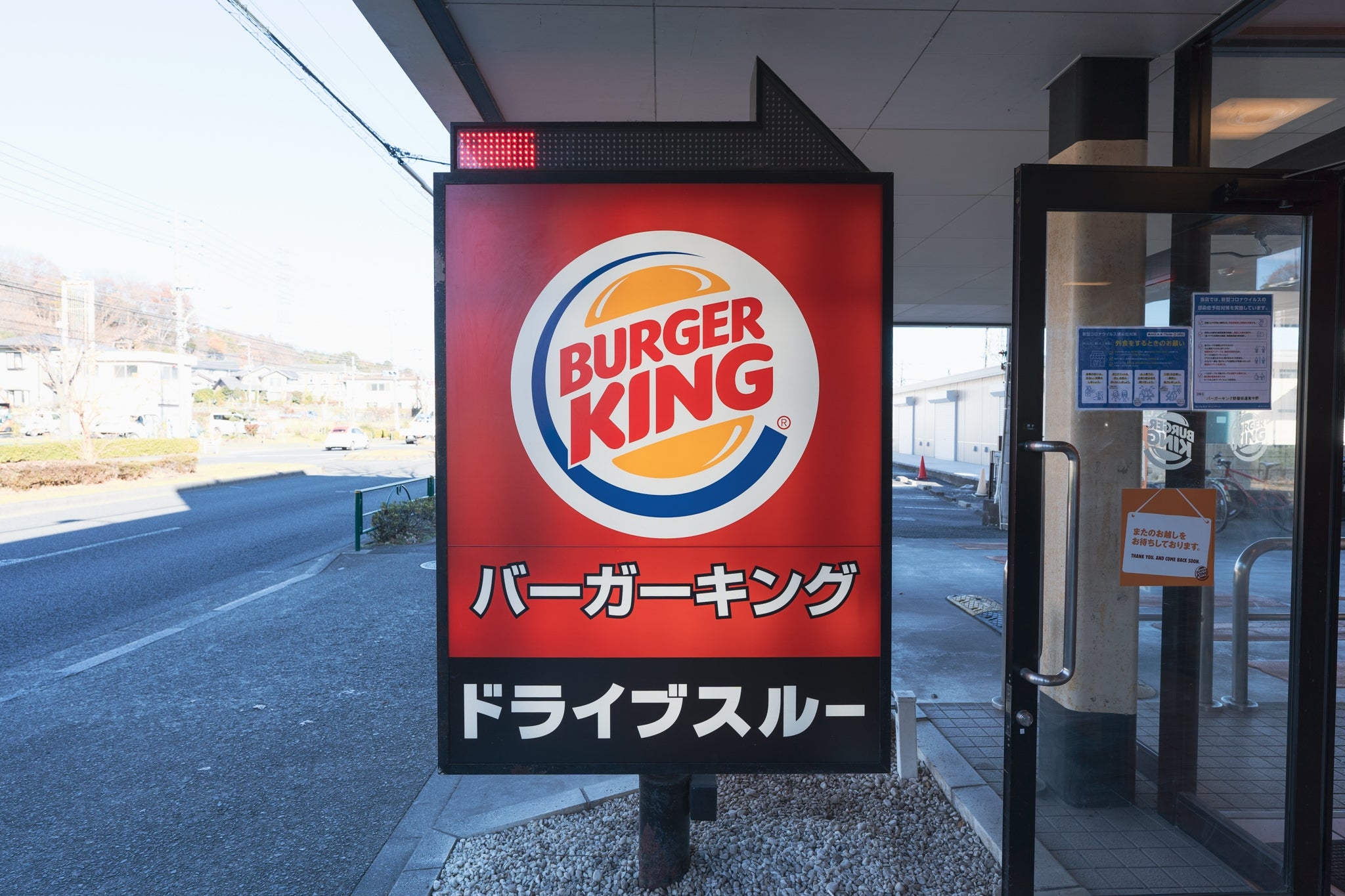 バーガーキングの看板が道路沿いに設置されている。ドライブスルーの案内が記載されている。