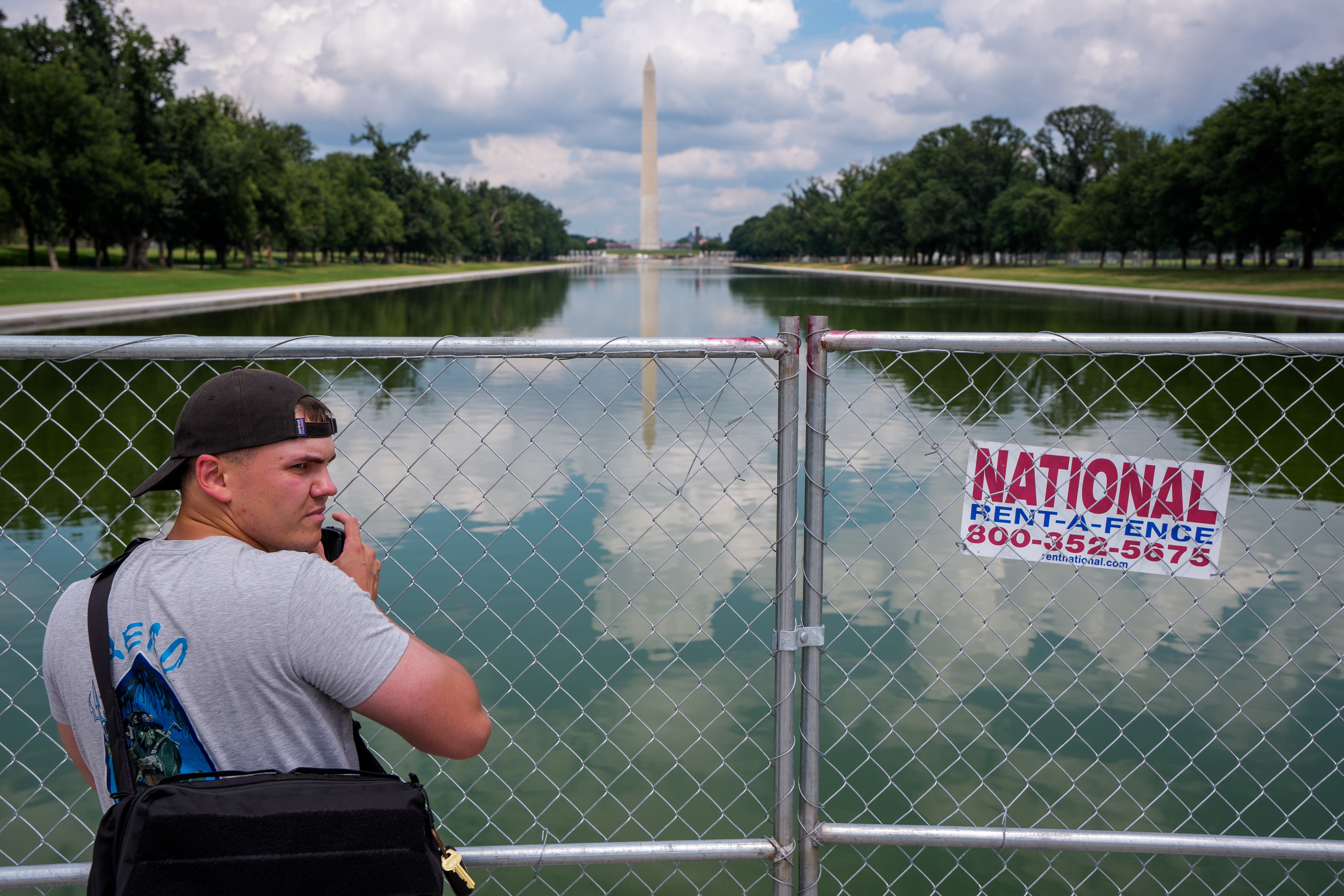 Person med walkie-talkie står ved et midlertidig gjerde nær det reflekterende bassenget, med utsikt over Washington-monumentet i bakgrunnen