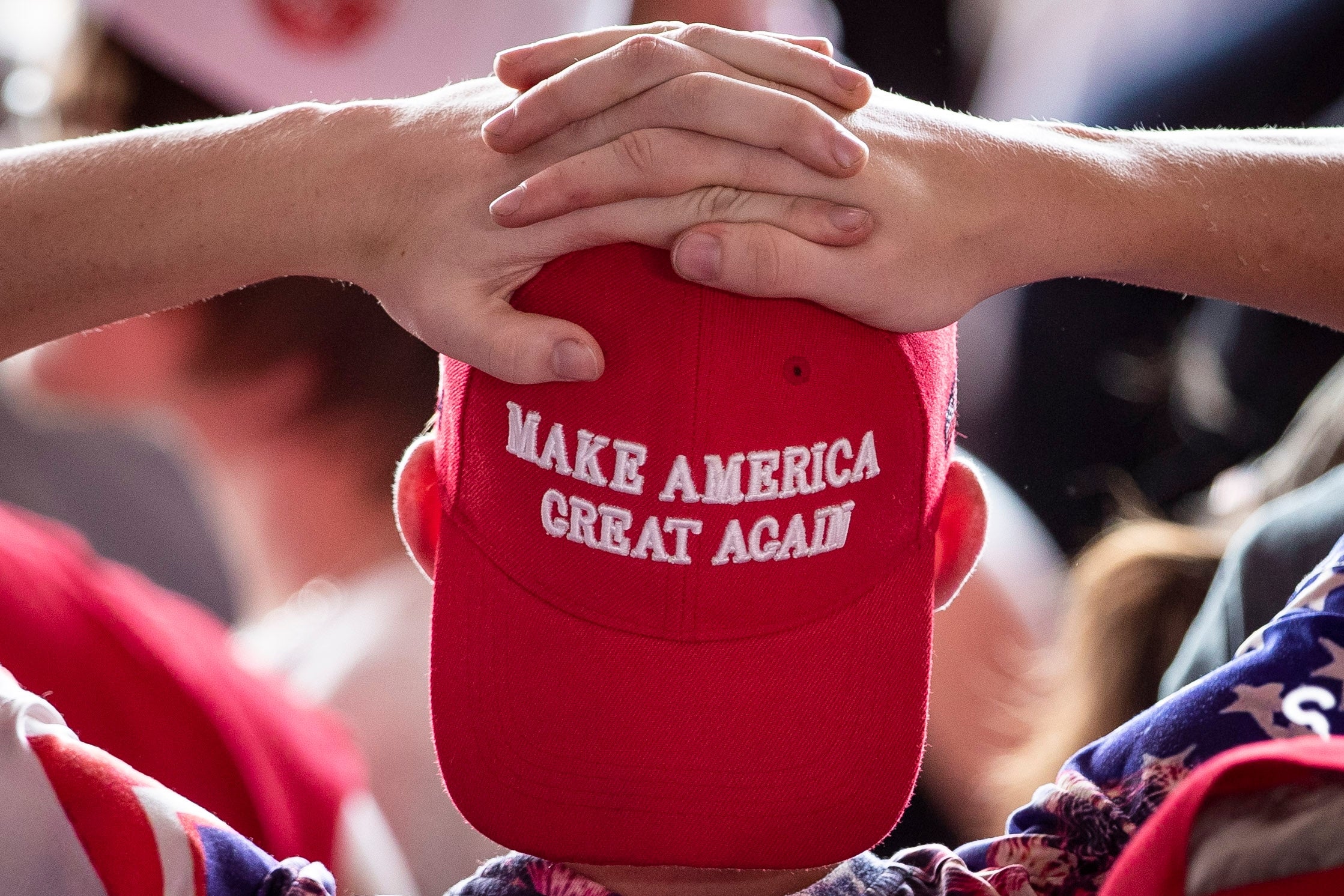 Person som har på seg en "Make America Great Again" caps med hendene knyttet bak hodet på et overfylt arrangement